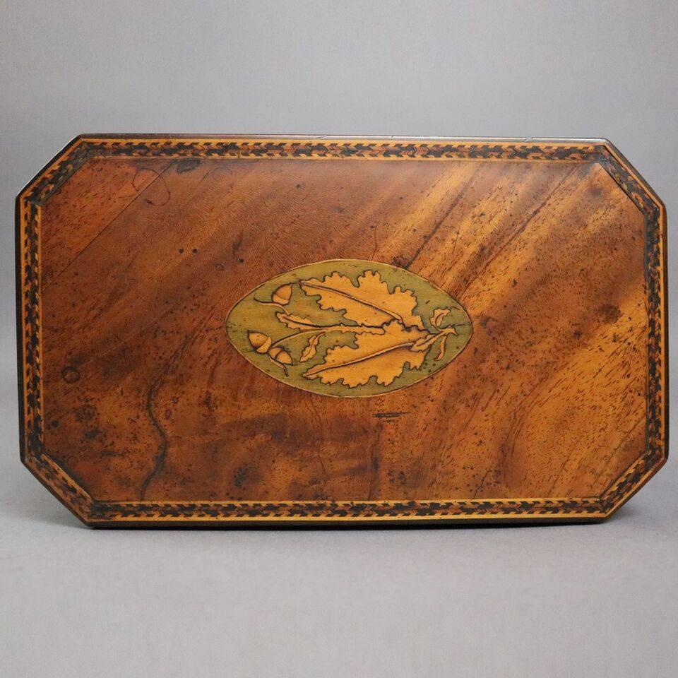 Antique English George III tea caddy features mahogany construction including two interior compartments, inlaid satinwood oak leaf on top and banding, bone escutcheon, circa 1790.

Measures: 5" H x 8.25" W x 4.75" D.