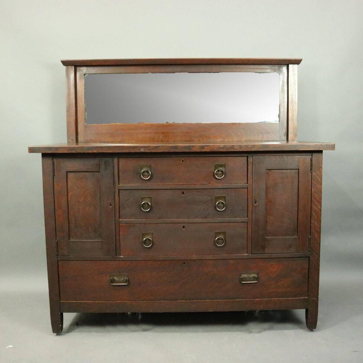 Antique Arts and Crafts mission oak Stickley Brothers sideboard with three central drawers flanked by storage cabinets above one long drawer, mirrored backsplash, bronze hardware, circa 1920.

Measures - 53.5" H X 54" W X 23.5" D,