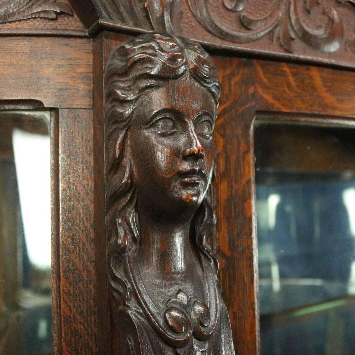 Antique china cabinet by R. J. Horner Brothers features quarter sawn and carved oak construction including caryatid, acanthus, rinceaux, and paw feet, curved glass front and sides, four interior glass shelves with mirror back display, circa