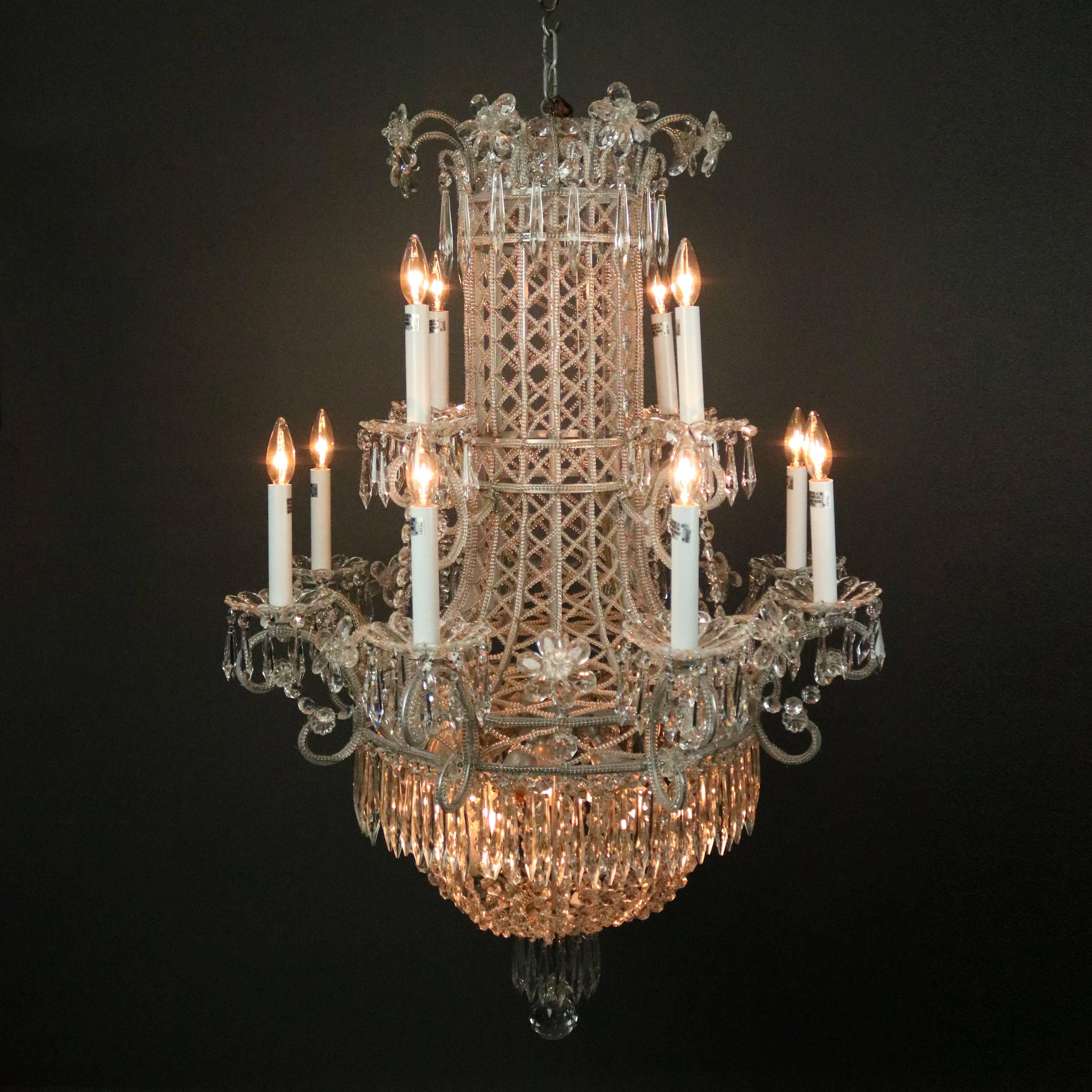 Oversized vintage French chandelier features twelve scrolled arms terminating in candle lights, strung cut crystal diaper pattern bodice, floral highlights and hanging cut crystals throughout, adjustable canopy chain, circa 1950.

Measures: 47