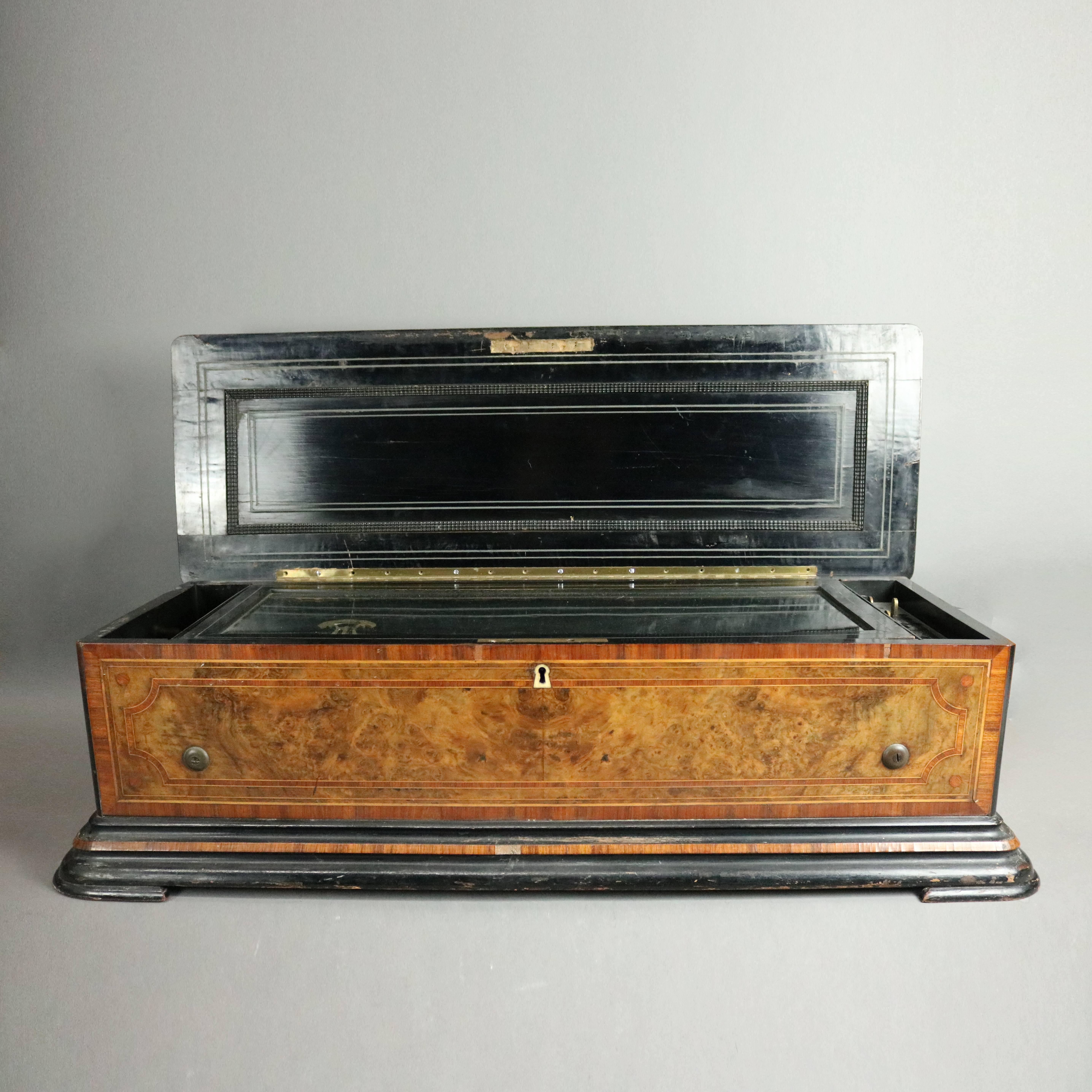 Antique Swiss cylinder music box plays twelve songs, housed in a burl mahogany case, ebonized and satinwood banded and inlaid, crank included, working condition, circa 1900

Measures - 10" H x 36" W x 12" D; 18.5" cylinder