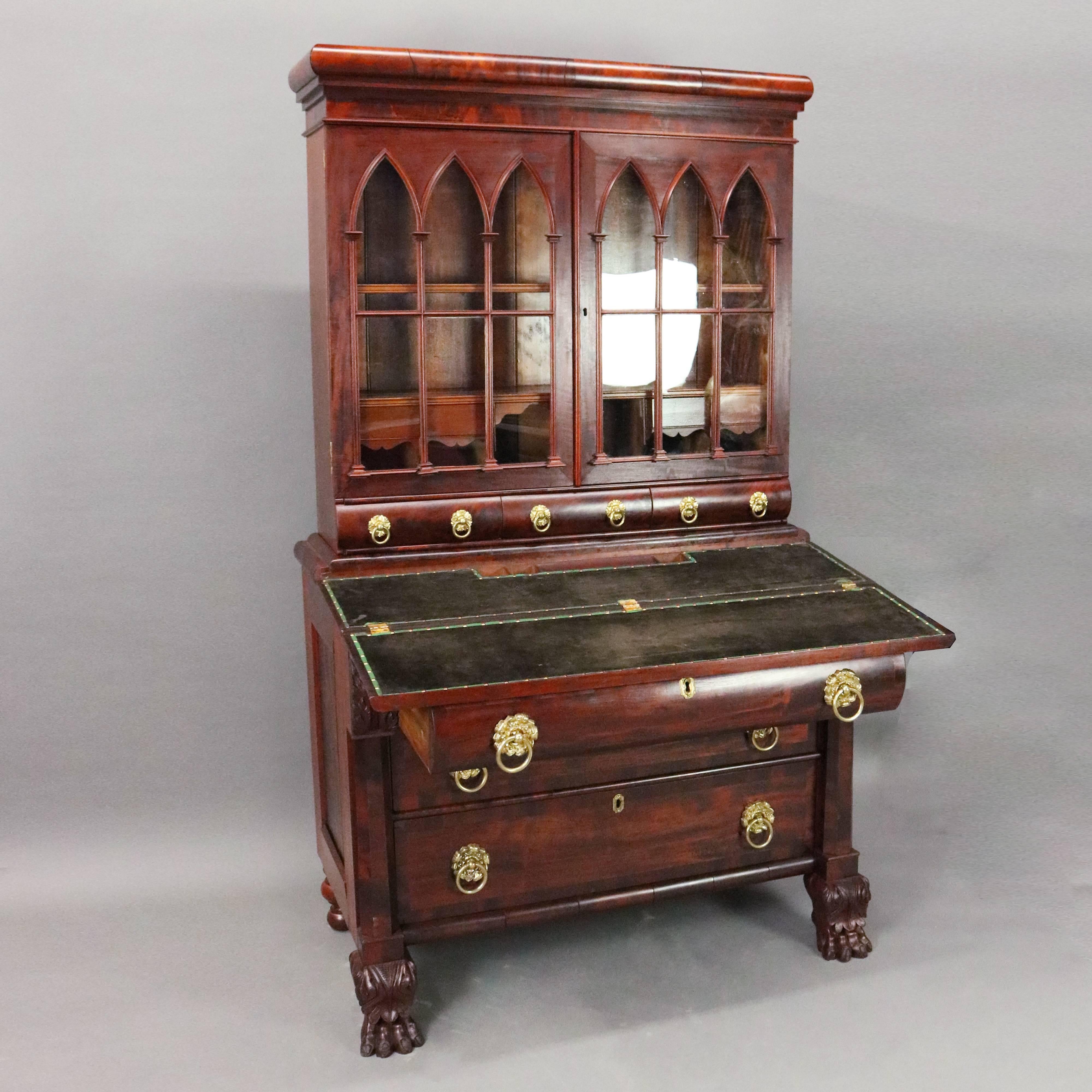 Antique American Empire secretary features flame mahogany construction with three long drawers in lower cabinet seated on highly detailed carved acanthus paw feet, leather flip top writing surface, all beneath bookcase with three small storage
