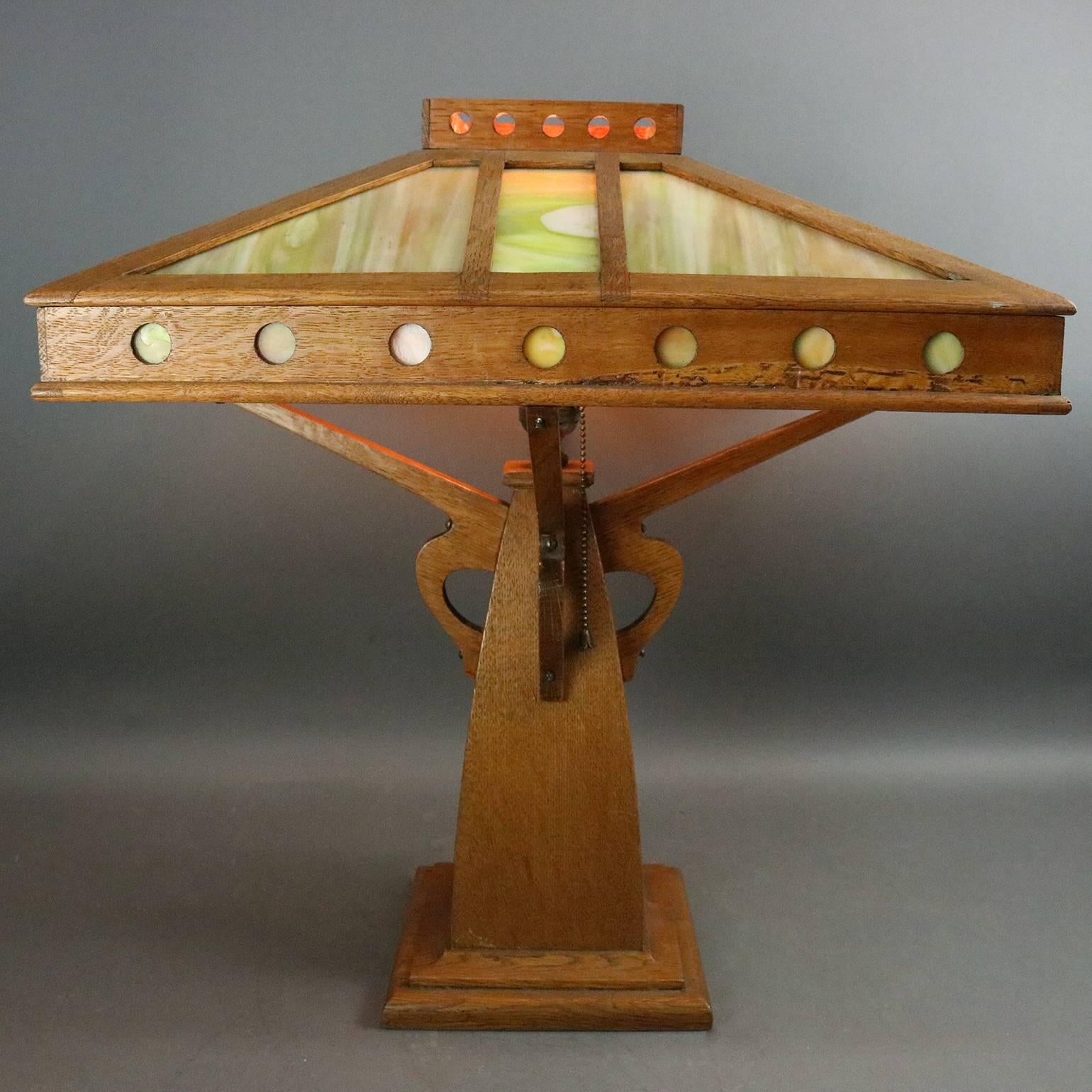 Oversized antique Arts & Crafts Prairie School table lamp by Peterson Art Furniture Co., Faribault, Minnesota, features mission oak construction with pierced oak shade with slag glass panels, supported by S-shaped supports, circa 1910

Measures: