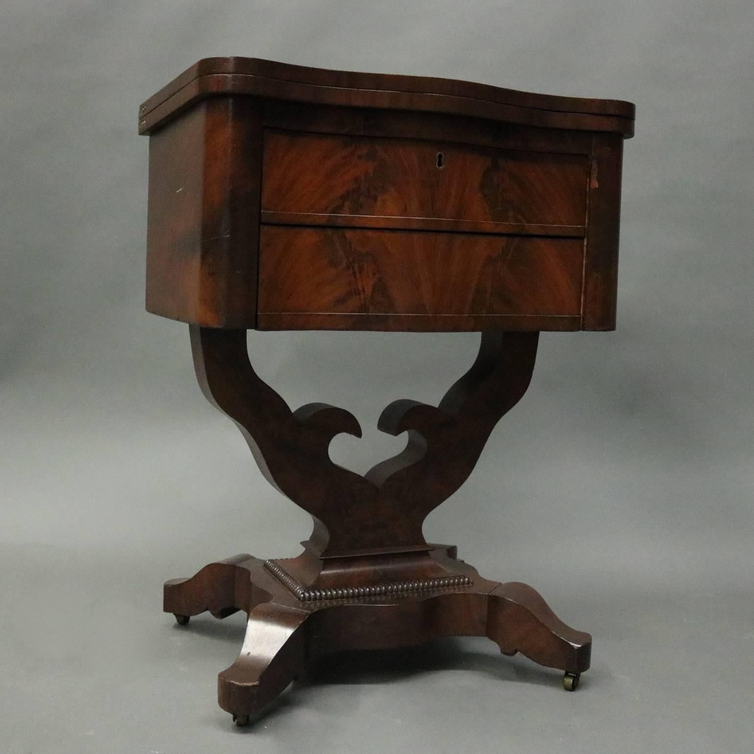 Antique flame mahogany American Empire sewing stand features serpentine front two-drawer cabinet atop open plinth, top opening and swivels to seat and provide work surface or game table, circa 1880.

Measures -30.5" H X 23" W X 16"