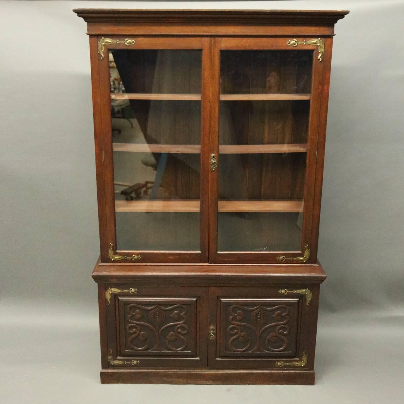 Antique Art Nouveau two-piece bookcase features mahogany construction with double door lower cabinet with stylized tree of life and foliate design carved panels, upper cabinet with double glass doors opening to shelved slat back interior, stylized