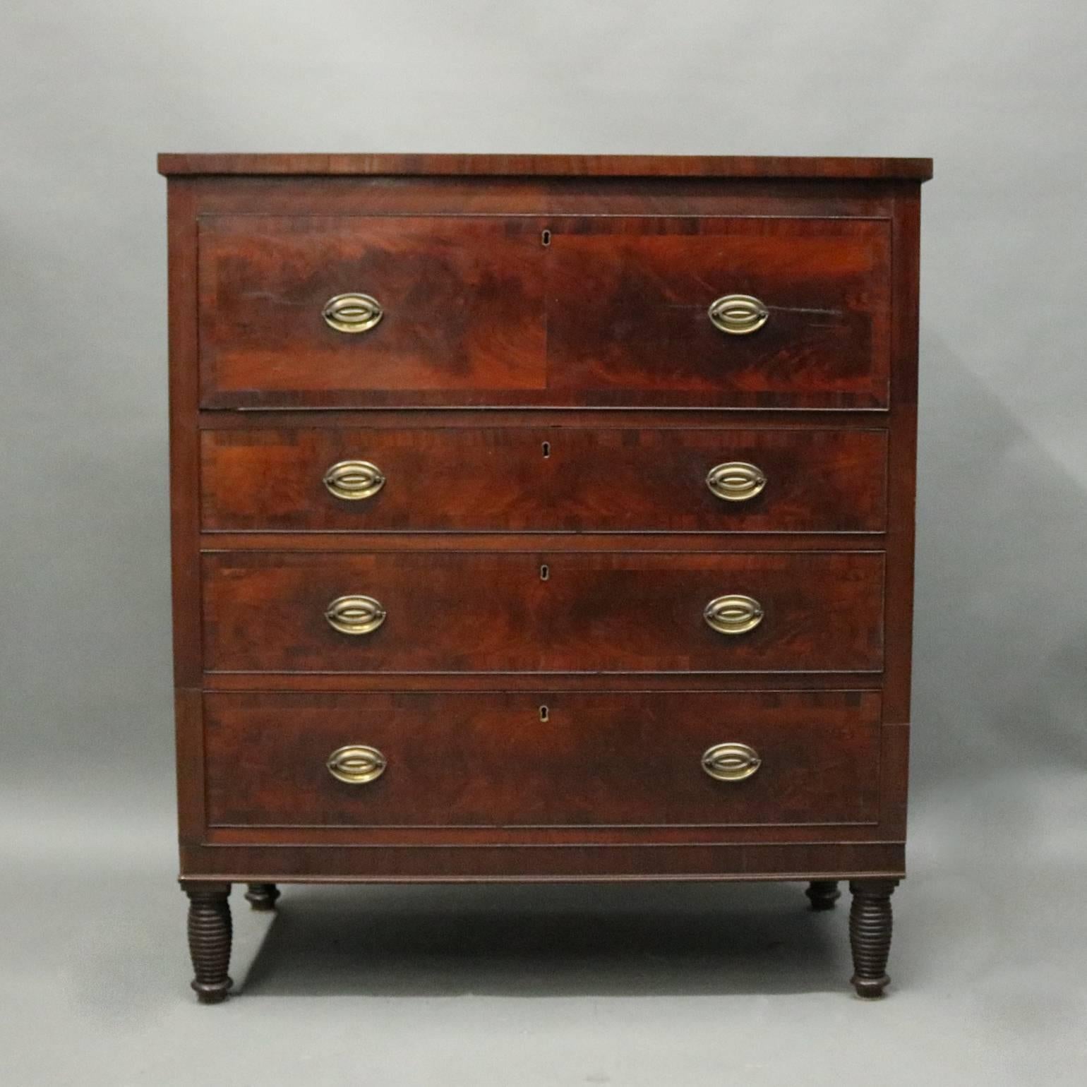 Antique Sheraton butler's desk features flame mahogany construction with cabinet of three long drawers and drop front opening to writing surface and internal compartments, bronze pulls throughout, seated on turned horizontally reeded legs, circa