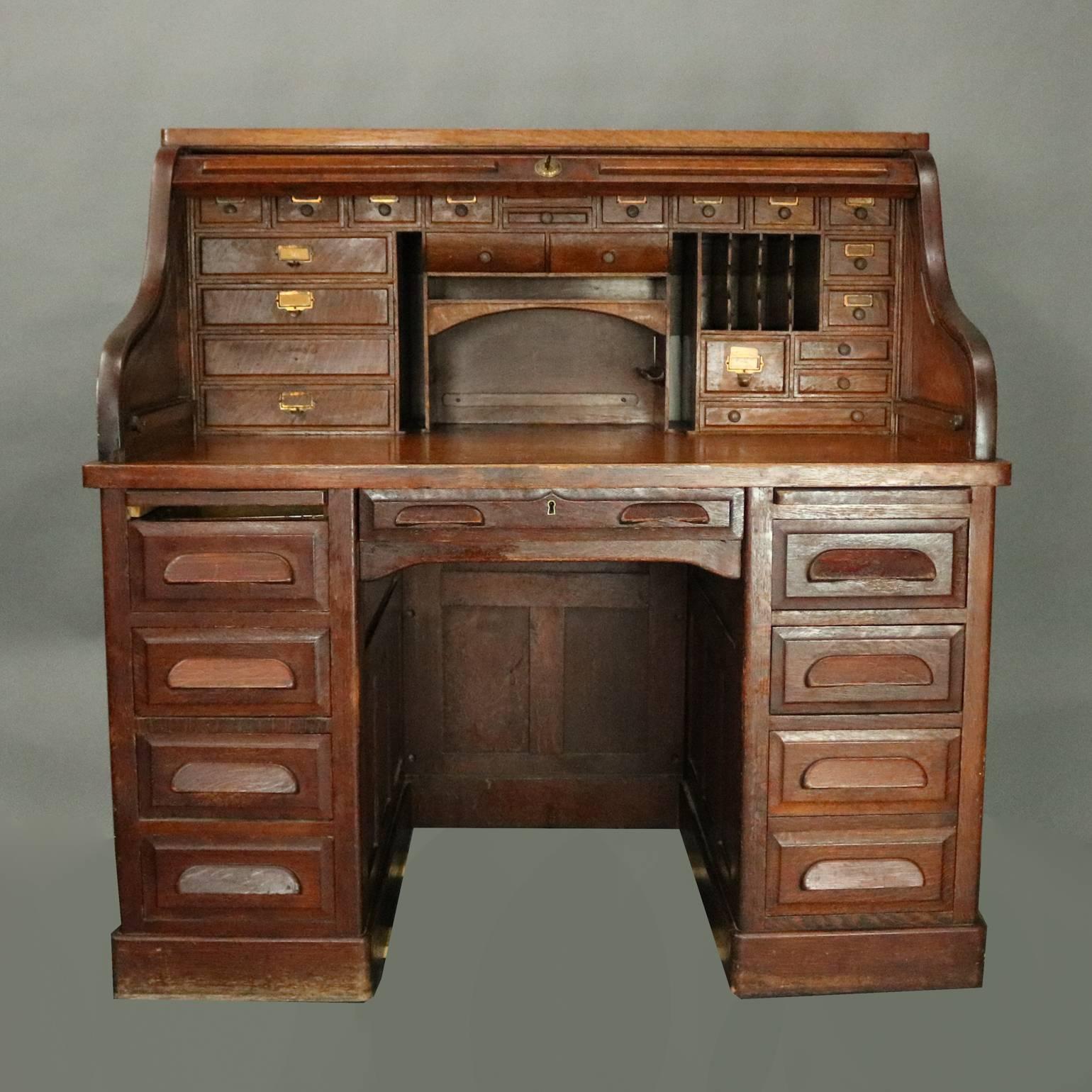 Antique roll top desk by The Standard Furniture Company features oak construction with raised panels on back and sides, knee hole with one long drawer and flanked by drawers and pull-outs, roll top opens to reveal sizable writing surface with