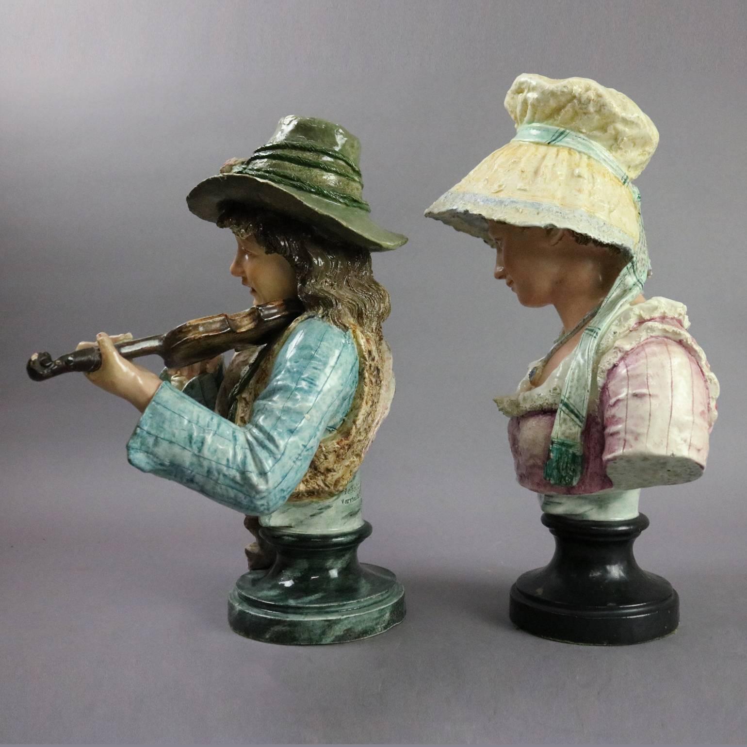 Pair of antique German Majolica earthenware pottery busts depict young woman wearing bonnet and young man musician playing violin, "Gesetzlich Geschutzt Vorbehalten 565 66" on pedestal on man, "536 70" on pedestal of woman, circa
