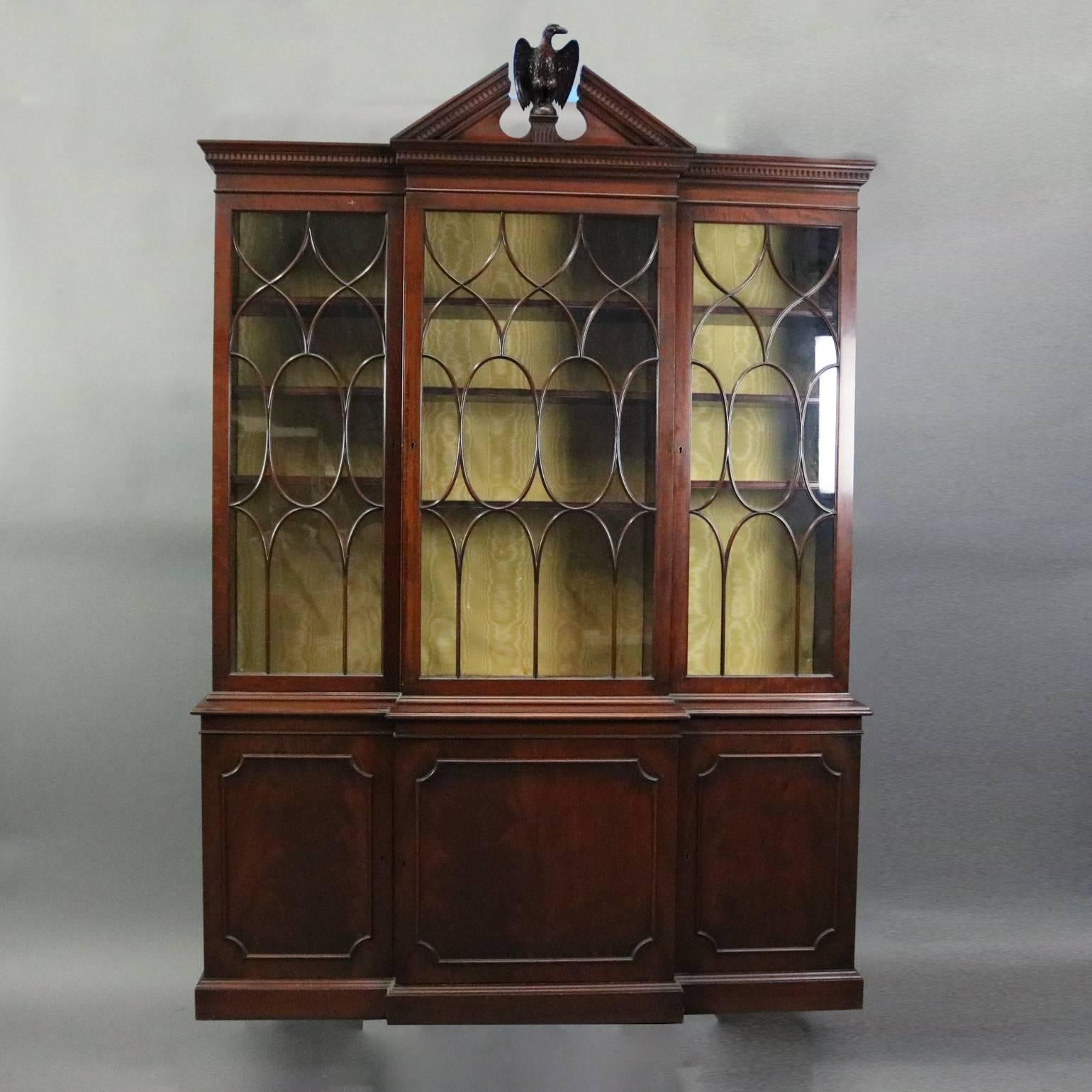 Antique Federal style two-piece breakfront china cabinet features mahogany construction with glass front doors opening to interior display, broken arch pediment with central carved eagle, includes two keys, en verso label reads "This piece was