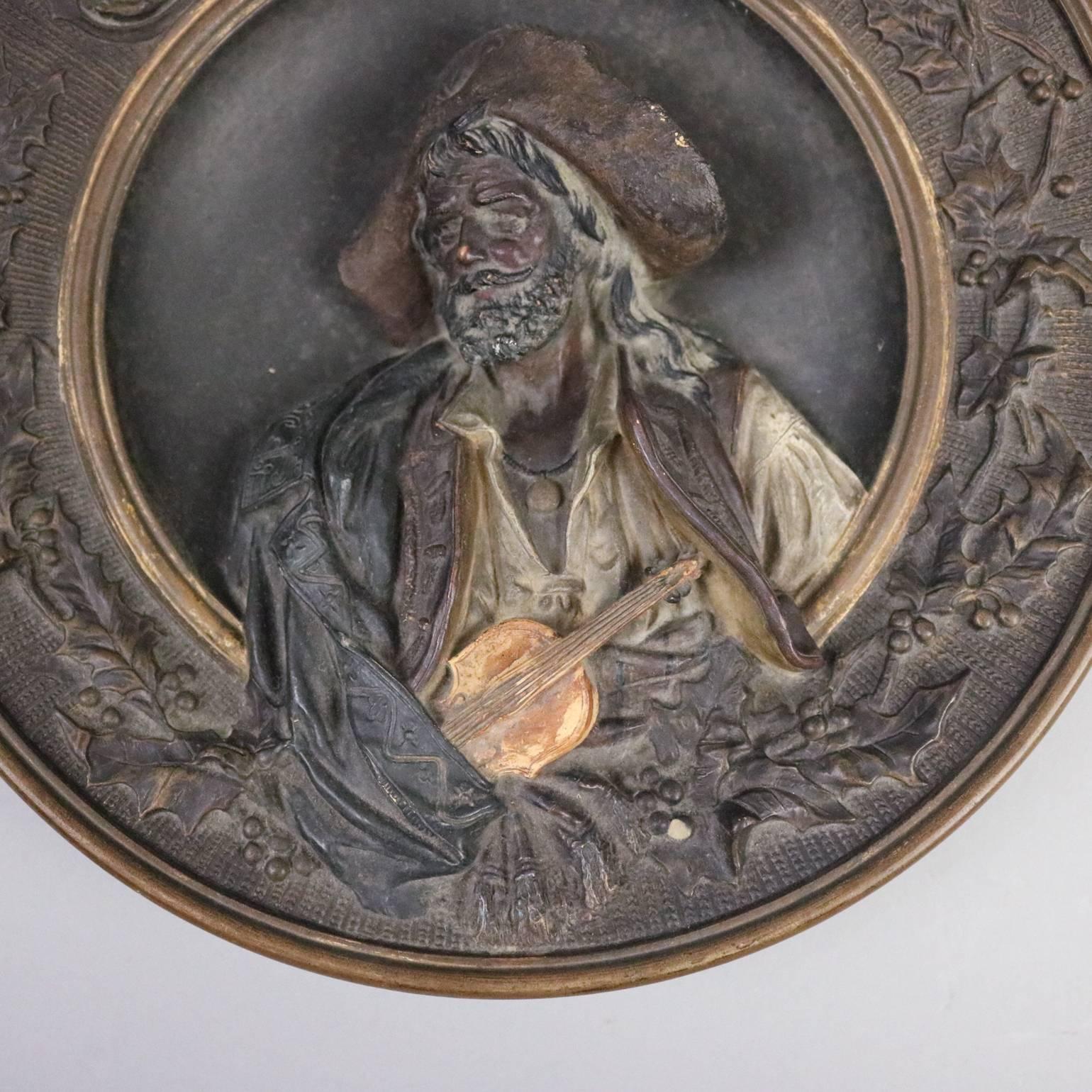 Antique Austrian high relief pottery plate by Musterschutz pottery depicts “Art et Liberte” (el violoniste), late 19th century, framed by wreath of holly, and incised en verso "Musterschutz 5746", circa 1880. This portrait after L. Gallait