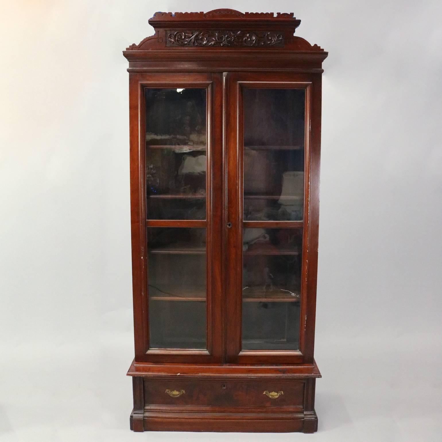 Monumental antique Eastlake walnut library or office bookcase features double glass doors opening to adjustable shelving, lower long drawer, incised and carved foliate acanthus crest, bronze hardware, circa 1880.

Measures: 86