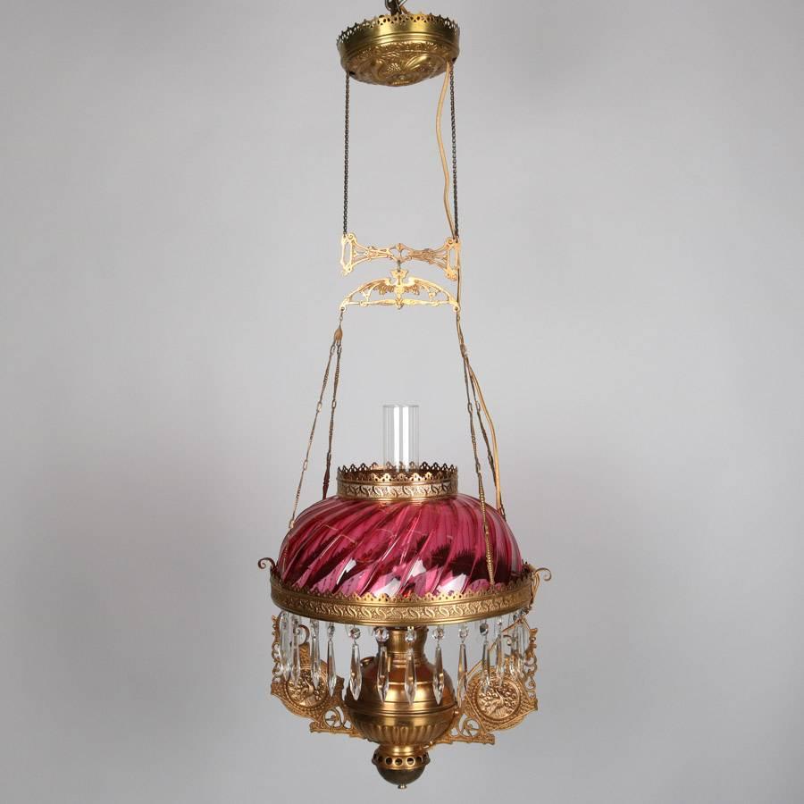 Antique hanging parlor lamp features pierced gilt cast frame with figural winged cat and scroll decorated flanking medallions with peacock reserves, cranberry glass shade and cut crystal prisms, electrified and rewired, 19th century.

Measures -
