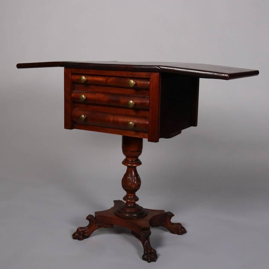 Antique American Empire flame mahogany drop-leaf side table features three-drawer case atop acanthus carved plinth and seated on four paw feet, 19th century

Measures: 30.75" H x 19" W x 17" D, 37" wide open.