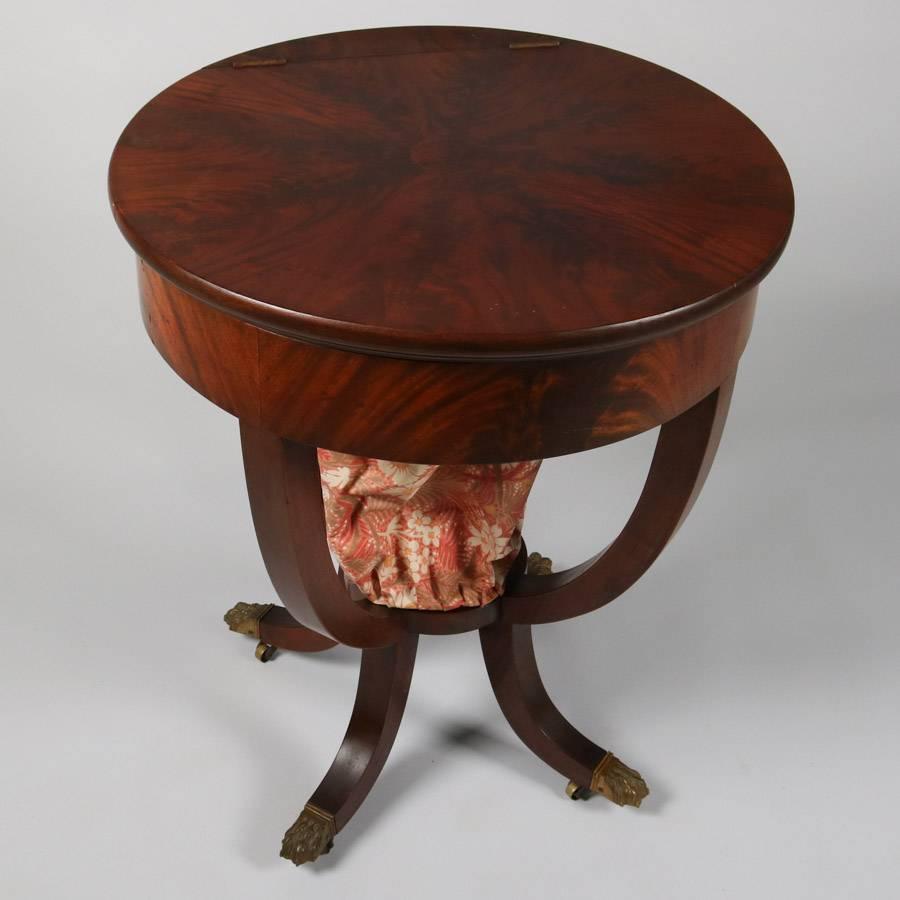 Antique American Empire Quervelle school sewing table features flame mahogany construction, sunburst top opens to reveal interior compartments and removable central bag, four splay legs terminate in cast bronze paw feet with casters, 19th