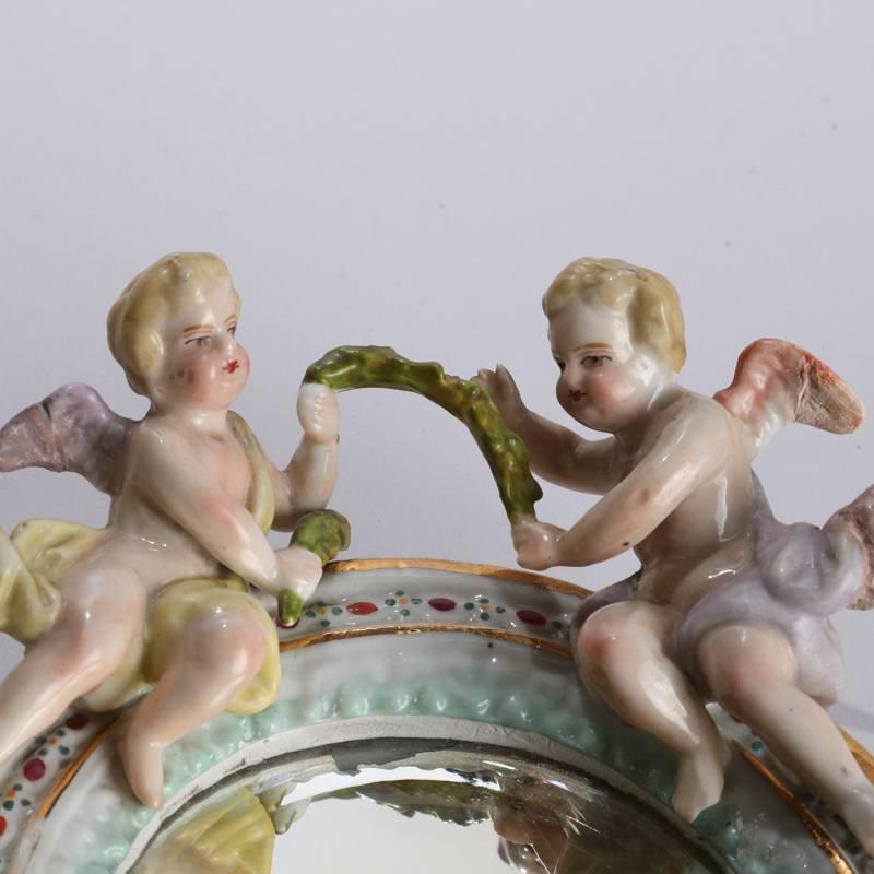 Antique German Meissen School figural porcelain vanity mirror features hand-painted and gilt frame with applied cherubs at crest and flowers below, bevelled mirror, top edge signed with blue underglaze "H", 19th century

Measures: