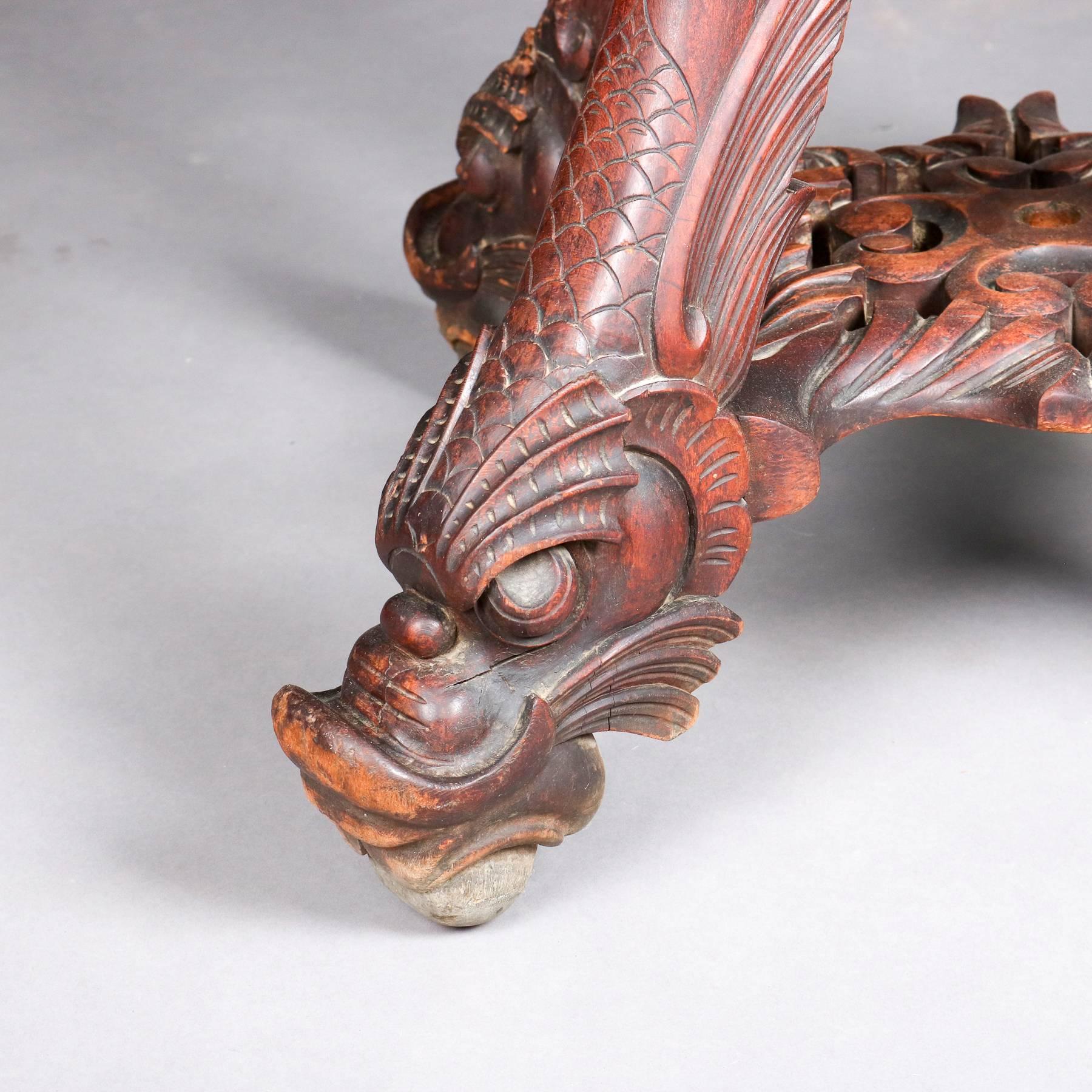 Antique Japanese Meiji plant/jardinière stand features turned upper display atop base of four legs with incised dragon panels and terminating in figural carved ancient dragon heads complete with scales and backswept wings, carved and pierced lower