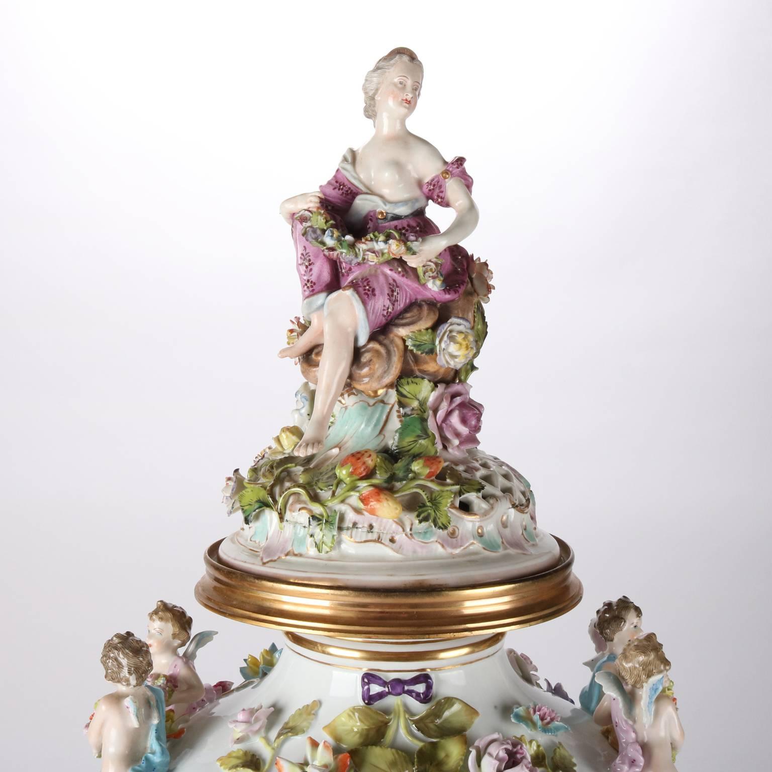 Monumental antique German Dresden figural porcelain urn features hand-painted reserve with courting scene, cherub handles, woman form finial, allover floral and foliate decoration, 19th century.

Measures - 30"H x 13.5"diam.