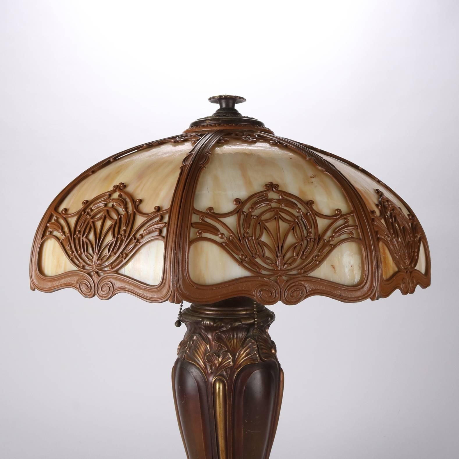 Antique Arts & Crafts table lamp by Bradley & Hubbard features filigree shade housing eight slag glass panels, three-socket base with cast bronze construction having foliate decoration and gilt highlights, signed on base, newly re-wired, 20th