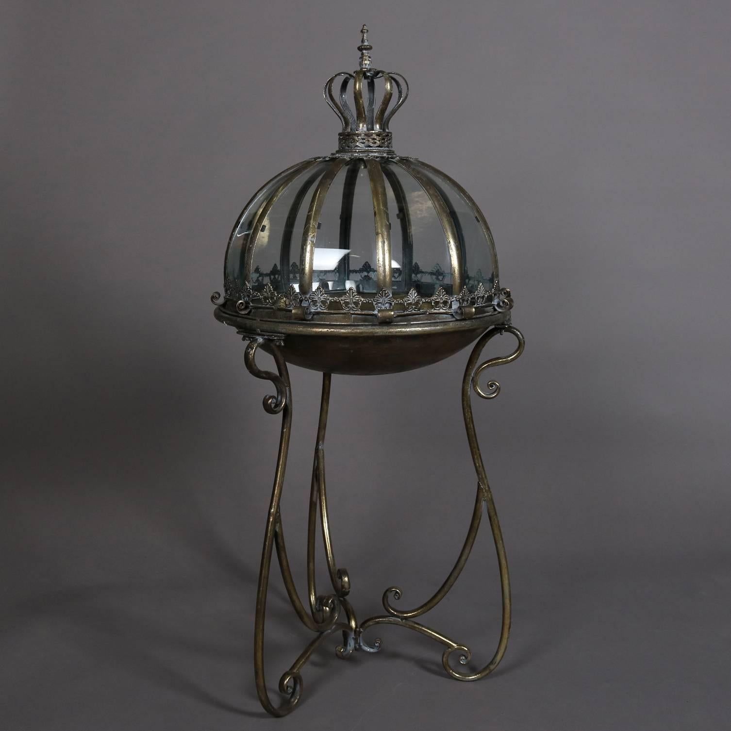 Hollywood Regency terrarium features scrolled metal stand with bowl supporting royal form domed glass cover reminiscent of king's crown, 20th century.

Measures: 40