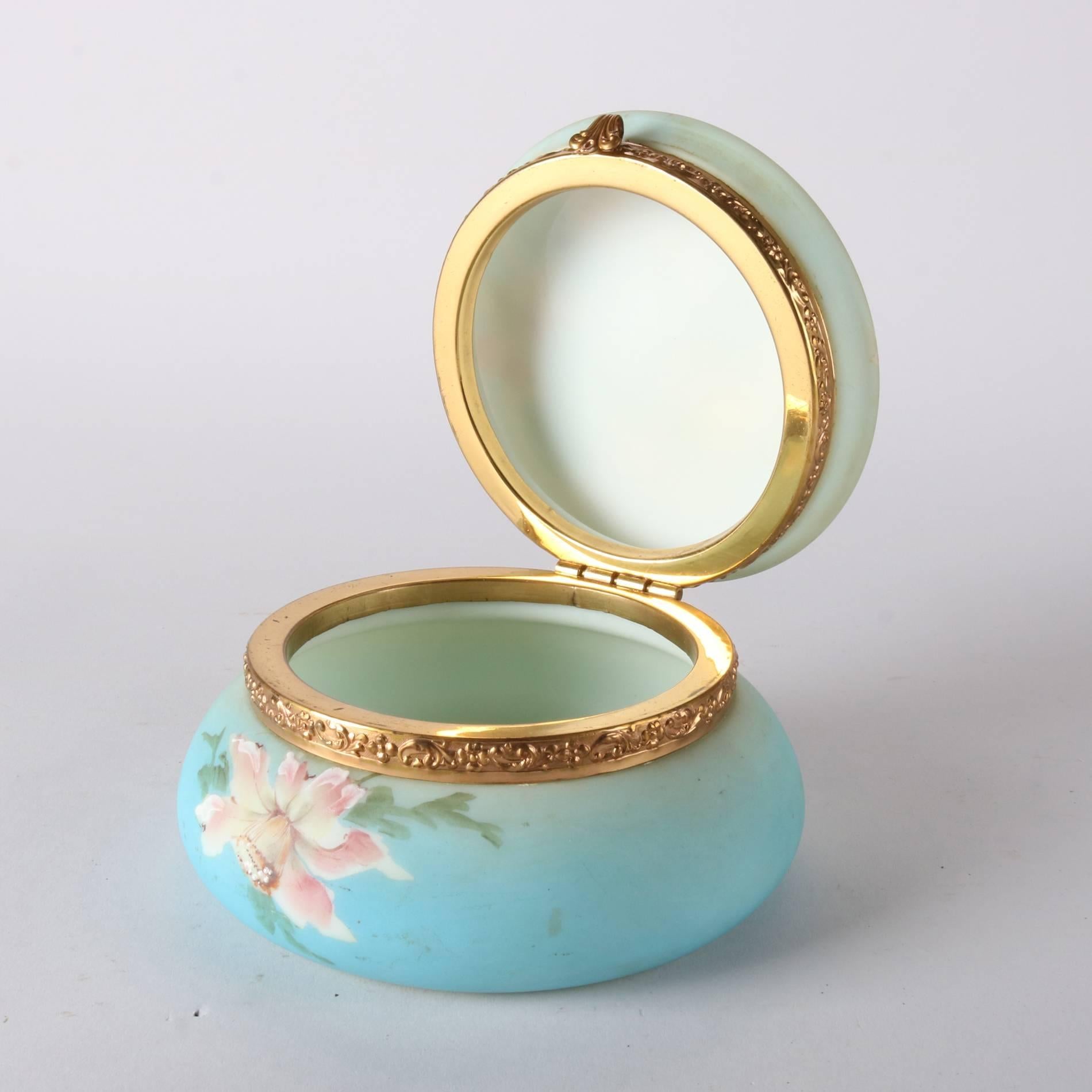 Antique Wavecrest School C.F. Monroe & Co. Nakara opal ware glass dresser jar features hand painted floral decoration, foliate embossed brass attachments, and is stamped on base, 19th century

Measures - 3.5"h x 6"diam