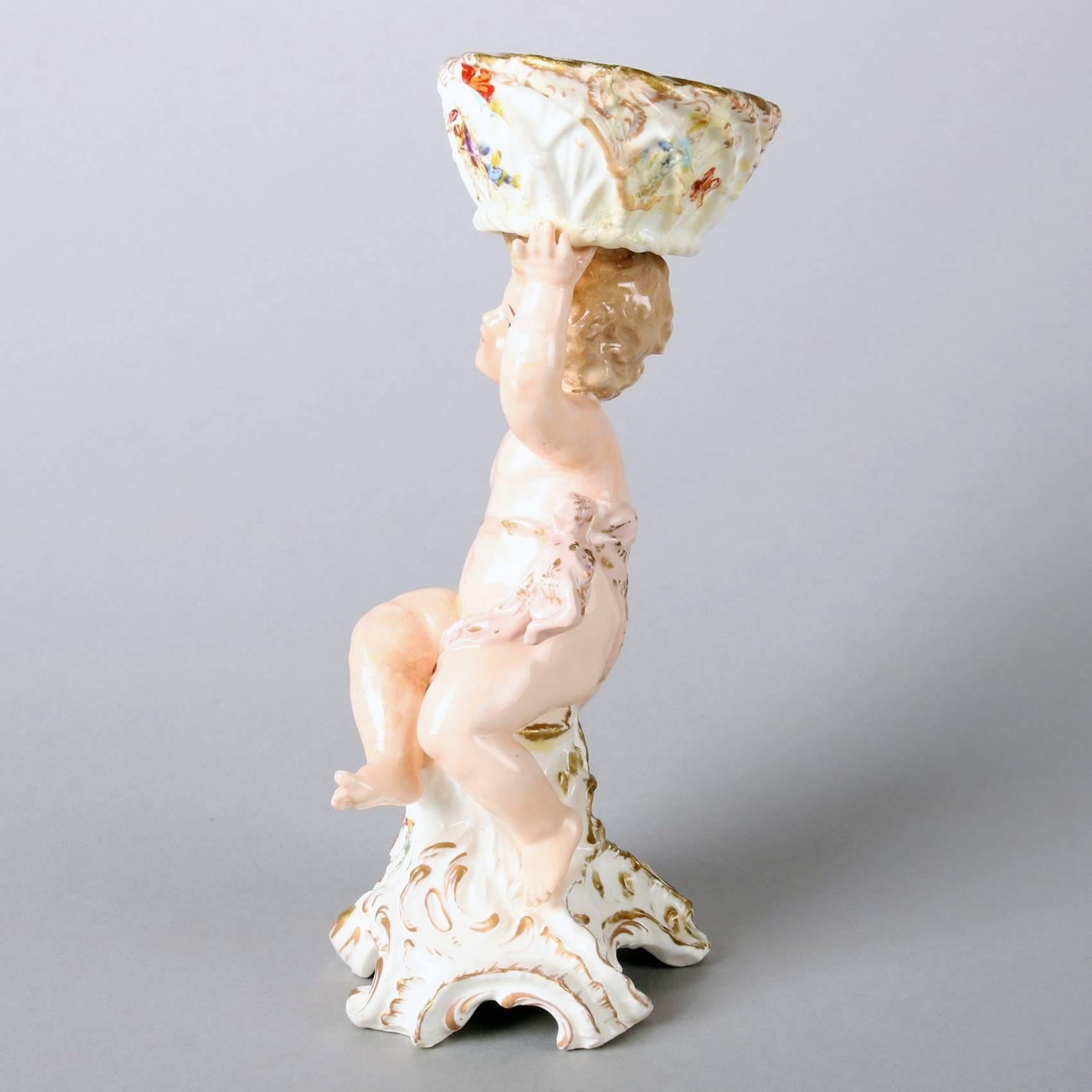 Antique German Meissen School figural porcelain compote features hand-painted cherub atop a Rococo style plinth and supporting a floral decorated basket, gilt highlighted throughout, 19th century

Measures - 9' H x 4.5