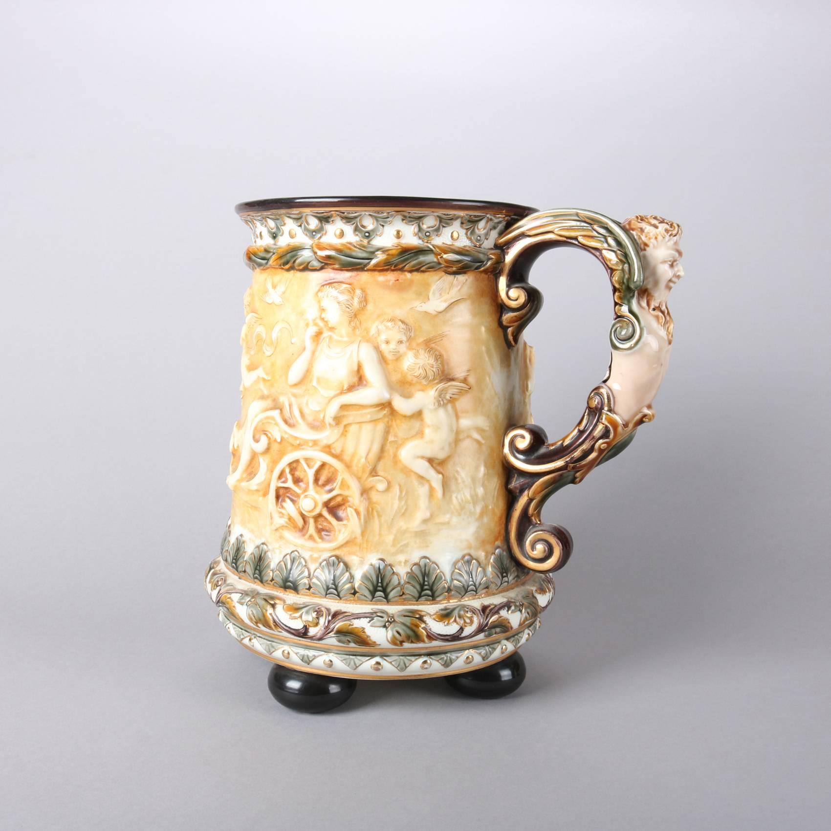 Oversized Swedish antique art pottery mug by Rorstrand features high relief Classical scene including cherubs and chariots, figural mask handle, and seated on ball feet, crown Rorstrand maker mark stamped on base with "Made in Sweden",