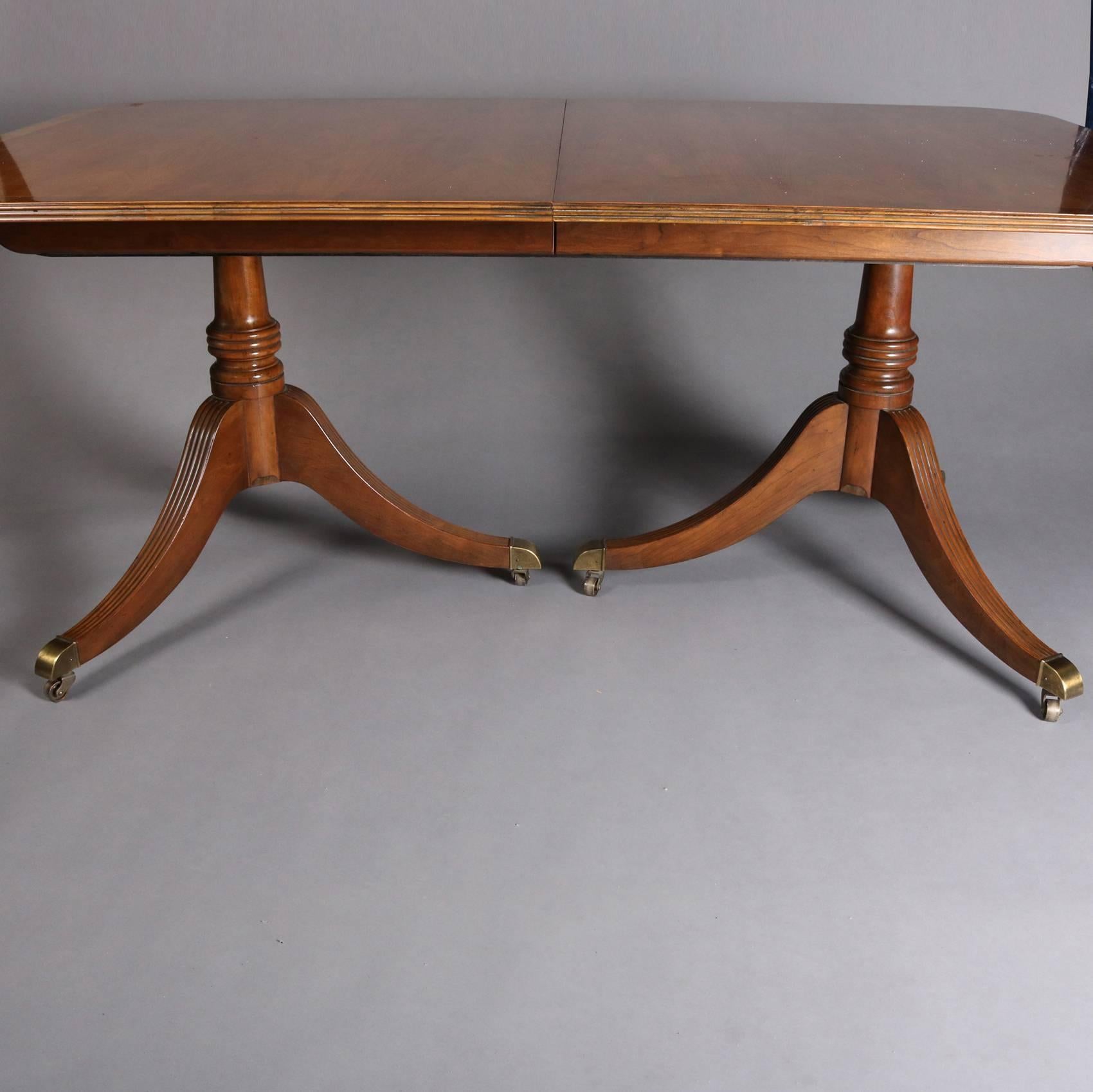 Vintage mahogany Duncan Phyfe style Baker School dining table features double pedestal seated on three bronze capped legs, with three 18