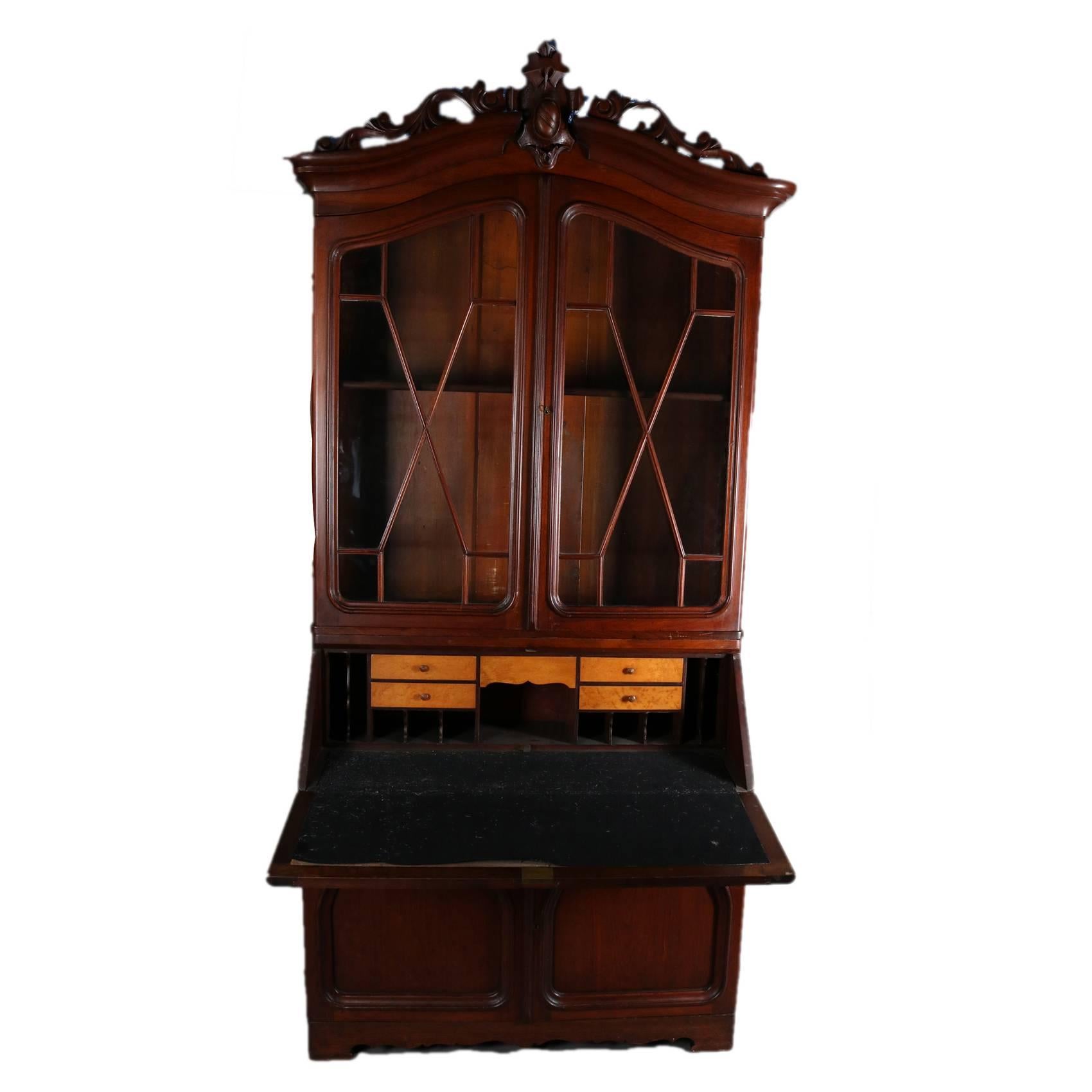 Antique Victorian walnut secretary features carved and pierced foliate crest, glass front bookcase, drop front desk opens to reveal felt writing surface, pigeon holes and drawers; lower doors with arched reserves and bordered by carved foliate