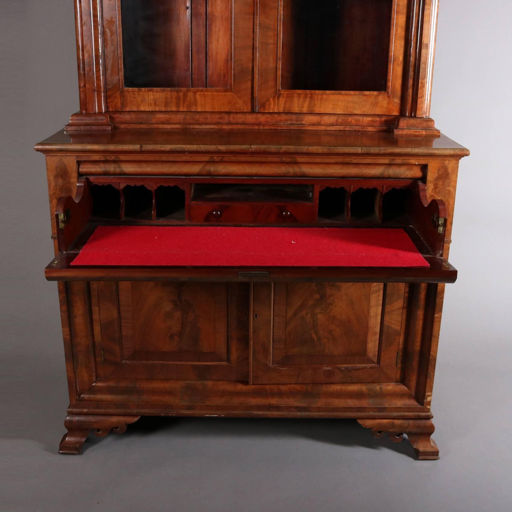 Antique Philadelphia American Empire flame mahogany secretary features upper glass front bookcase with pierced stylized floral corner pieces, drop front opens to reveal felt lined writing surface and interior storage pigeon holes and drawer, lower