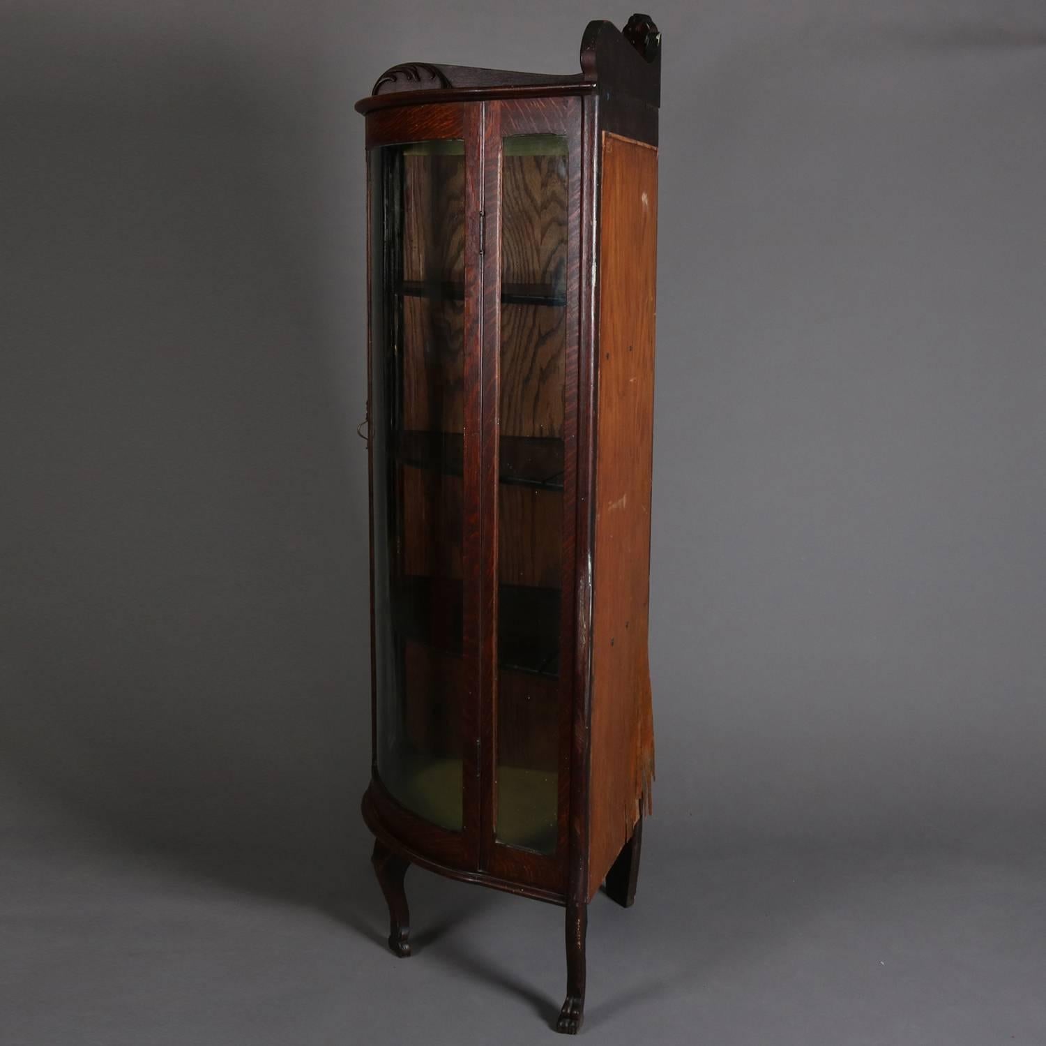 Antique R. J. Horner School oak corner china cabinet features carved foliate decoration and are seated on paw feet, single curved glass door open to fixed shelved interior with plate reservoirs, circa 1900.

Measures: 67