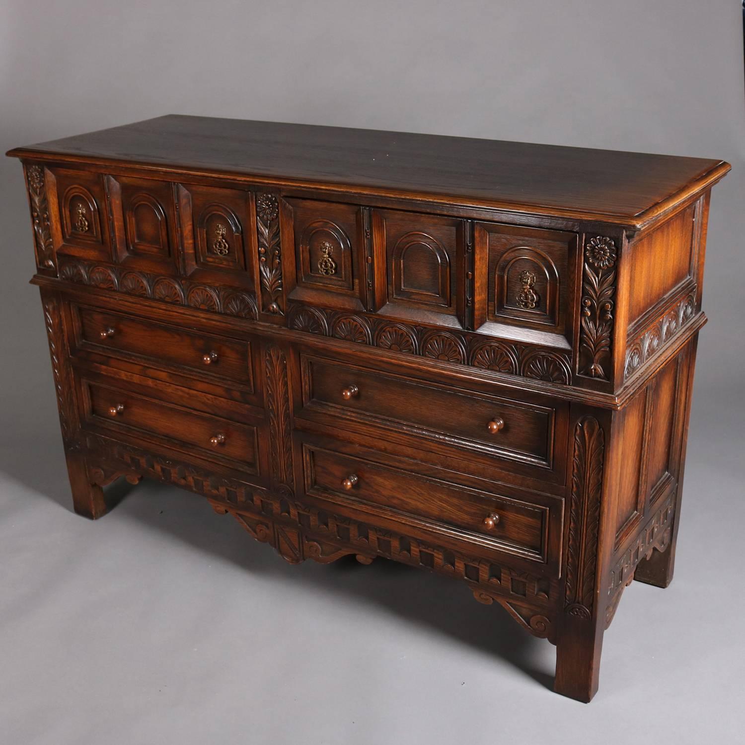 Antique Edwardian oak server features Jacobean influence with heavily carved sunburst and foliate bordering, paneled sides and front including arched reserves in upper drawers, and scrolled skirting, en verso original Kittinger Furniture tag, circa