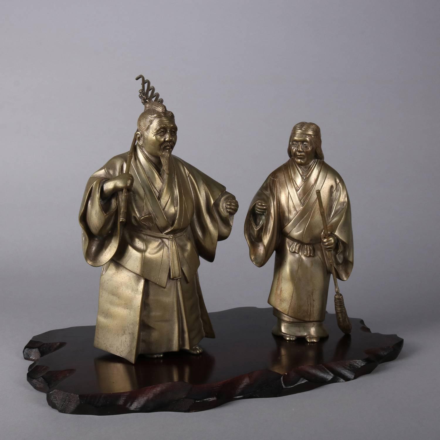 Set of Japanese figural bronzed sculptures feature the mythical figures of Jo and Uba, one with rake and the other with broom, wooden base dedication reads from United China & Glass Co. (Japan), larger sculpture with embossed chop mark signature as