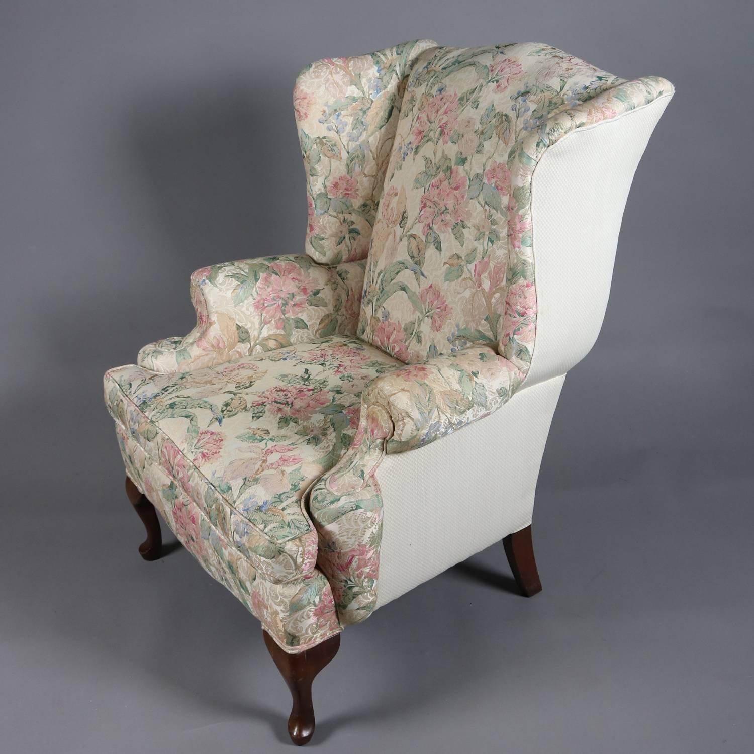 Pair of Queen Anne style wingback chairs feature flared backs, scroll arms, shaped apron and seated on mahogany Queen Anne legs; floral upholstered fronts with solid backs; 20th century

Measure: 42