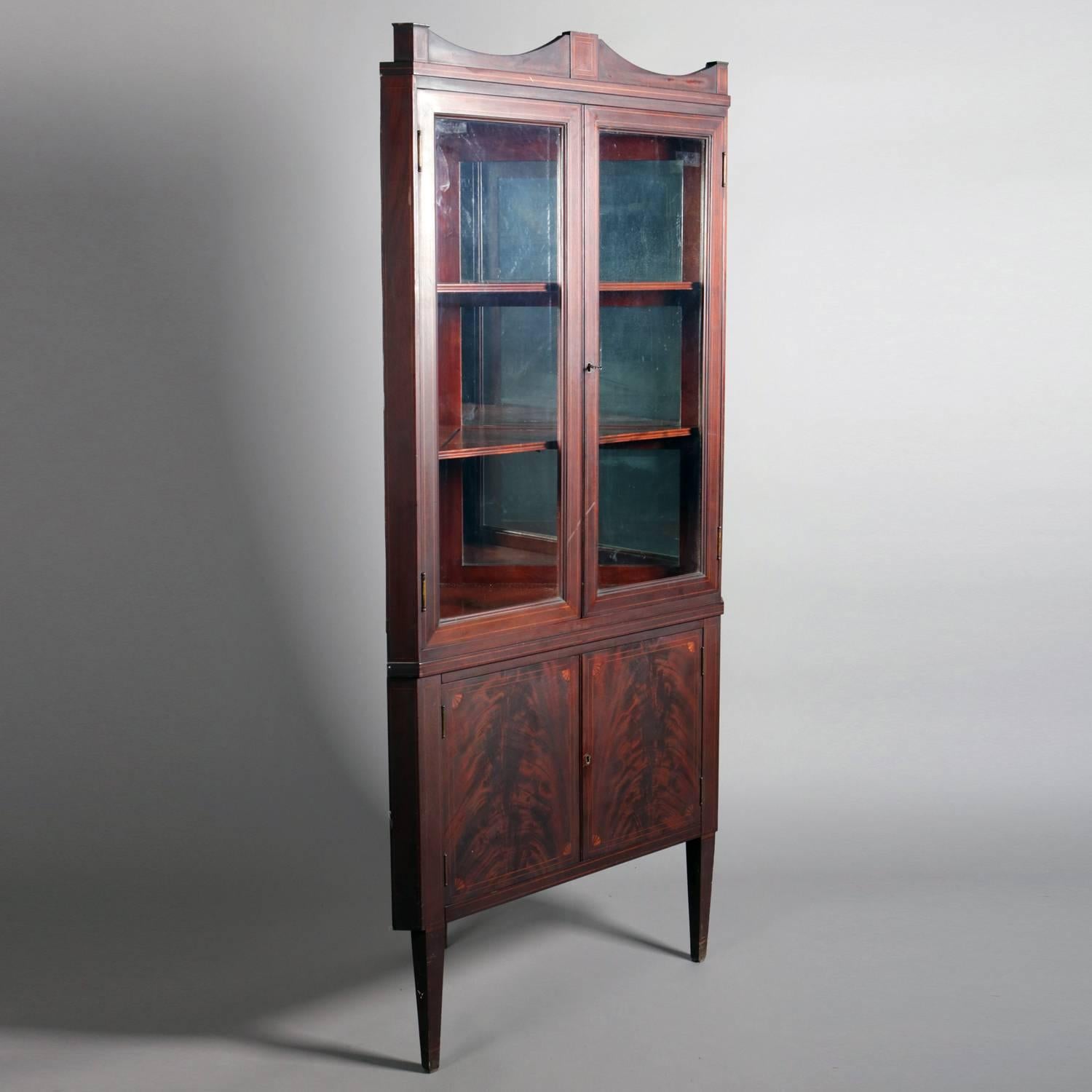 Vintage George III mahogany corner cupboard by Geo. C. Flint & Co., New York, features upper with double glass doors opening to fixed shelved and mirrored interior; lower with deeply striated flame mahogany double doors with satinwood inlay and