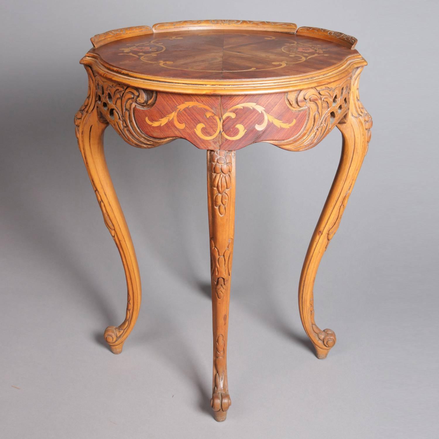 French carved yew wood occasional tea table features bookmatched mahogany top with floral and scroll marquetry and carved backsplash, foliate carved and pierced apron with satinwood scroll rinceaux inlaid mahogany reserve, and seated on carved