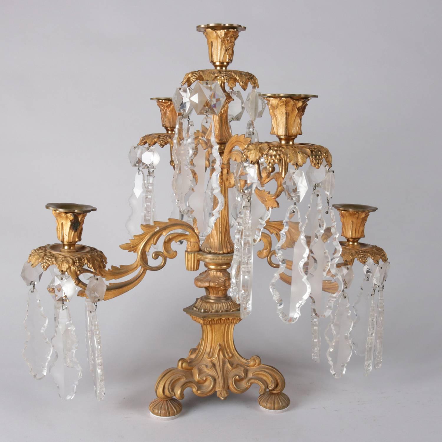 Antique Italian Baroque Cornelius School gilt cast bronze candelabra features four scroll and foliate form arms terminating in cut crystal prism decorate sconces with single central sconce, seated on tripod base with scroll form legs and reeded ball