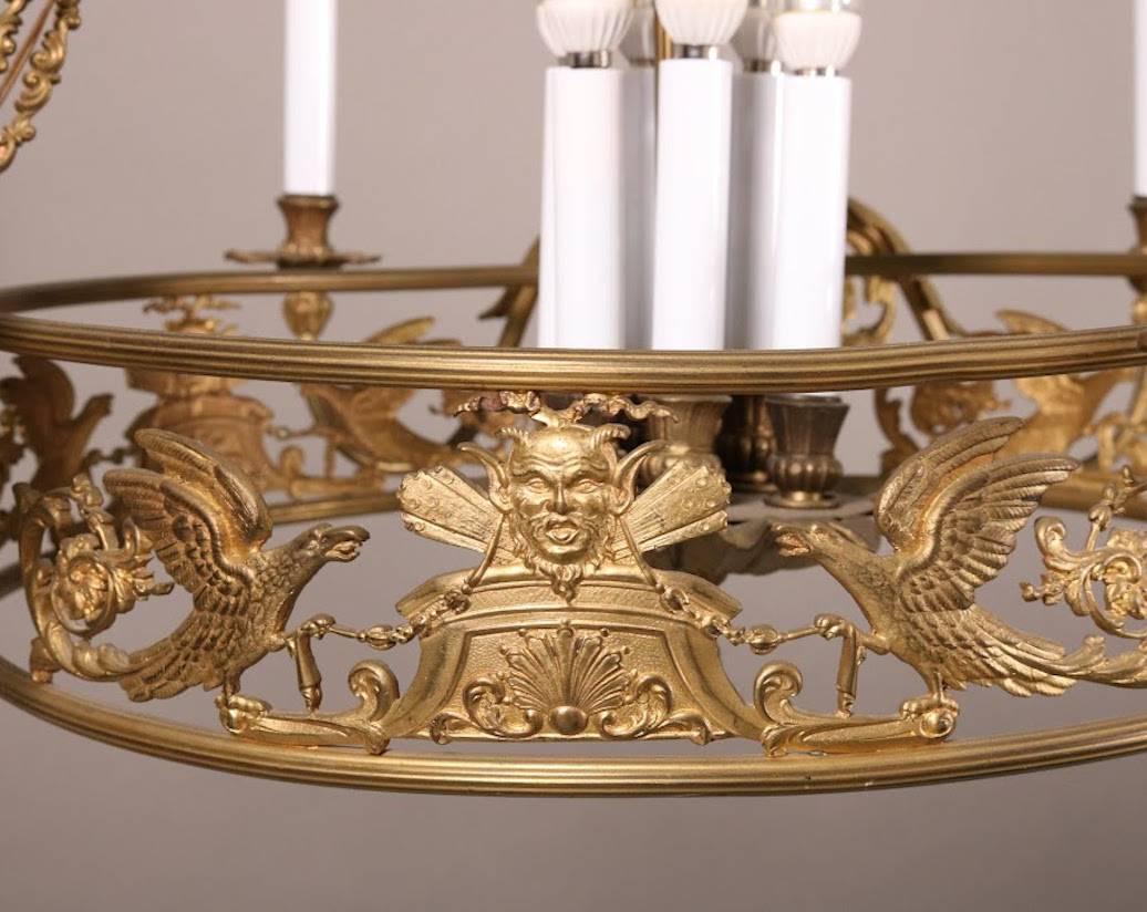 French Empire Classical ten-light figural chandelier features pierced bronze collar with phoenix and masks, six scroll and foliate arms terminating in candle lights, four candle lights surrounding central column, late 19th century.

***DELIVERY