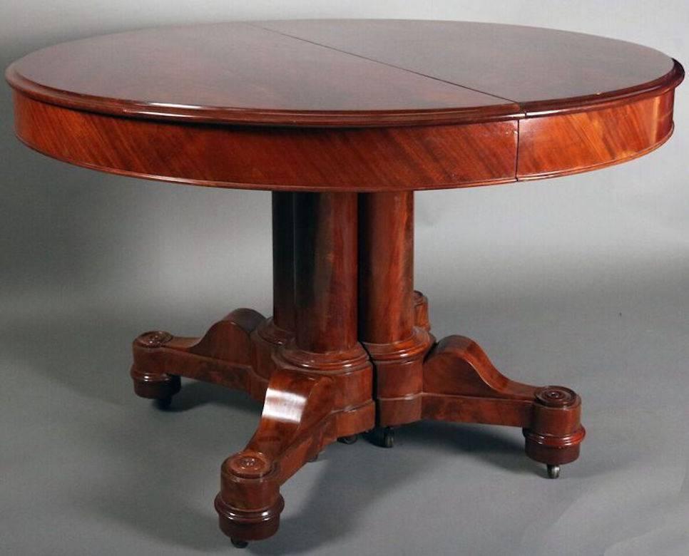 Rare American Empire flame mahogany dining table features clustered split column with corbel architectural elements on each leg terminating in classical roundels, French polish, three leaves, and center leg support. Design in the manner of Anthony