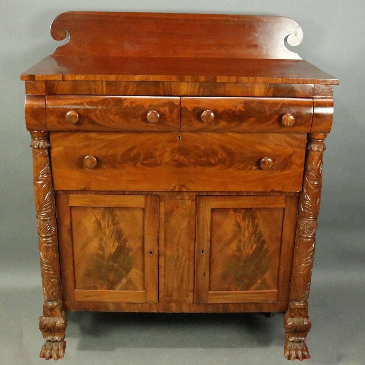 Antique American Empire Jackson Press features mahogany construction with flame mahogany cabinet flanked by acanthus carved columns terminating in paw feet, two convex upper drawers above one long drawer, en verso label reads The Linus & Fenn