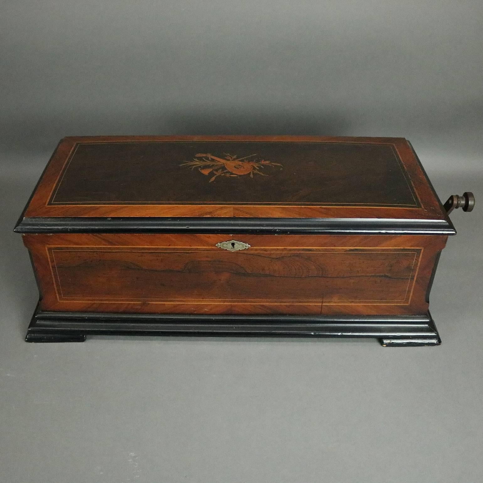 Antique Swiss cylinder music box plays 12 songs, housed in a double handle mahogany case, ebonized and satinwood banded with top inlaid with musical instruments (lute and horn), crank included, working condition, circa 1900

Measures: 9" H x