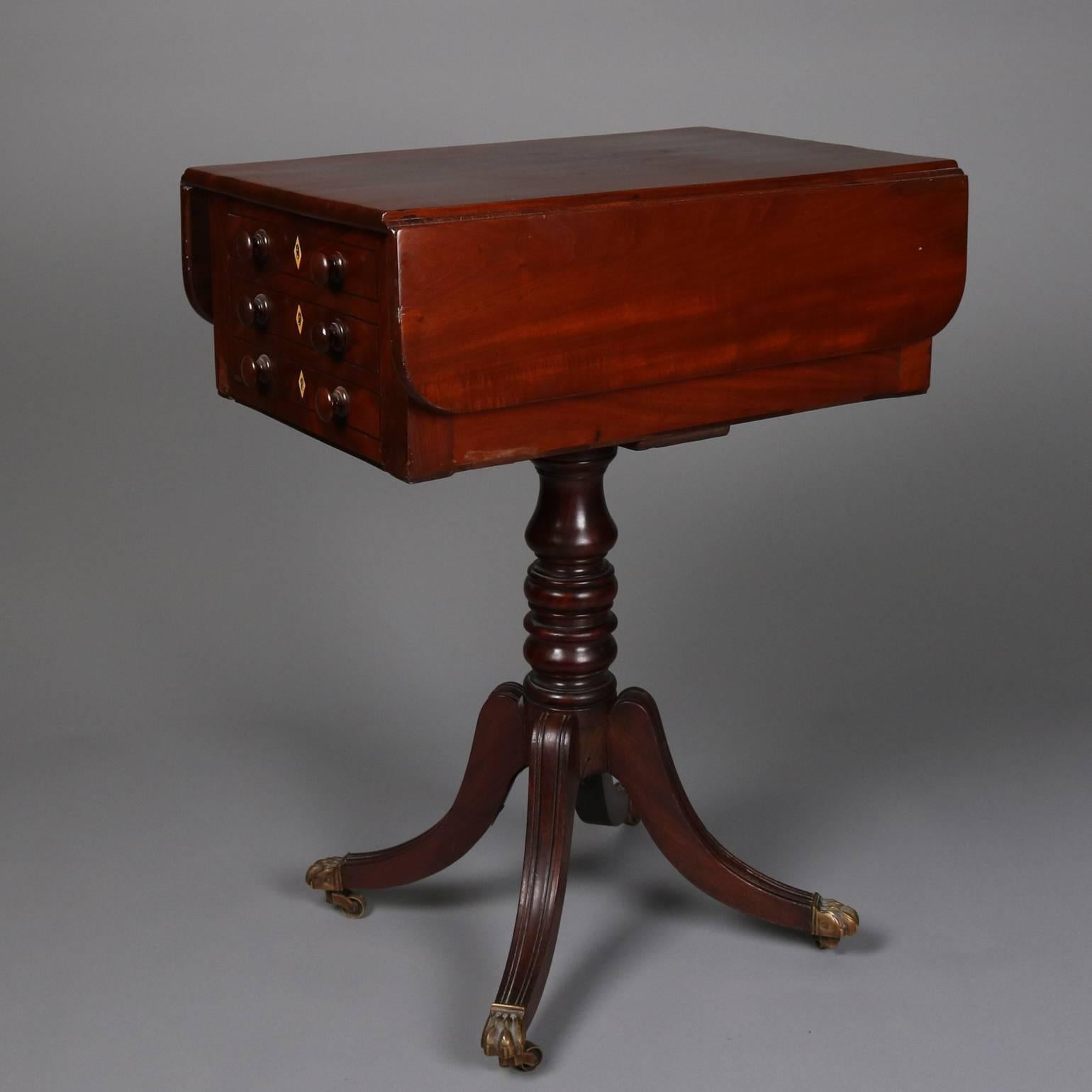Antique flame mahogany Duncan Phyfe School sewing Stand features three drawer case with inlaid bone escutcheons and drop leaf top above reeded splayed legs capped with cast bronze claw feet and casters, circa 1820

Measures: 28