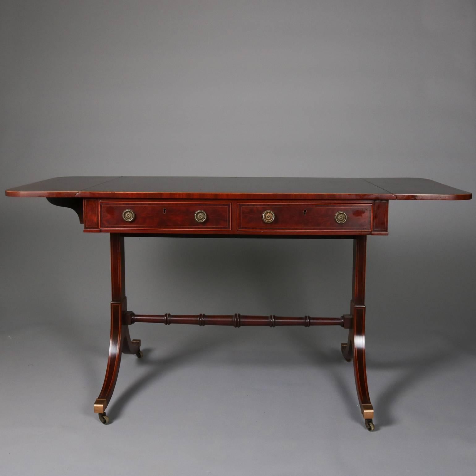 Antique English flame mahogany Duncan Phyfe school drop-leaf trestle server features two locking drawers with satinwood inlaid banding, splay legs connected with turned stretchers bronze caps and casters, en verso faux drawers, key included, 19th