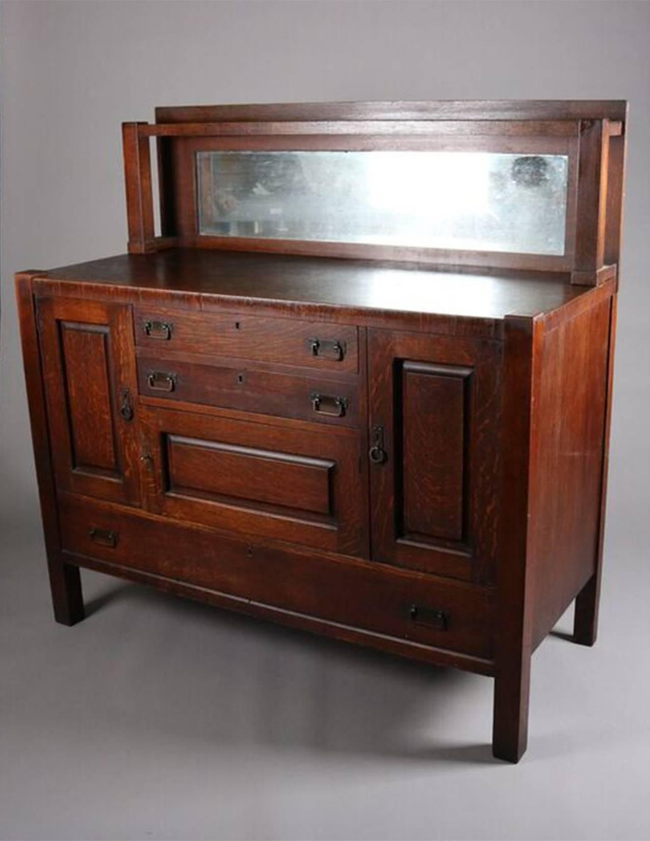 Antique Arts & Crafts Mission oak sideboard features mirrored backsplash above case with two center drawers and cabinet flanked by side cabinets and above a single long drawer, circa 1910

Measures: 54.5" H x 53.5" W x 24" D.