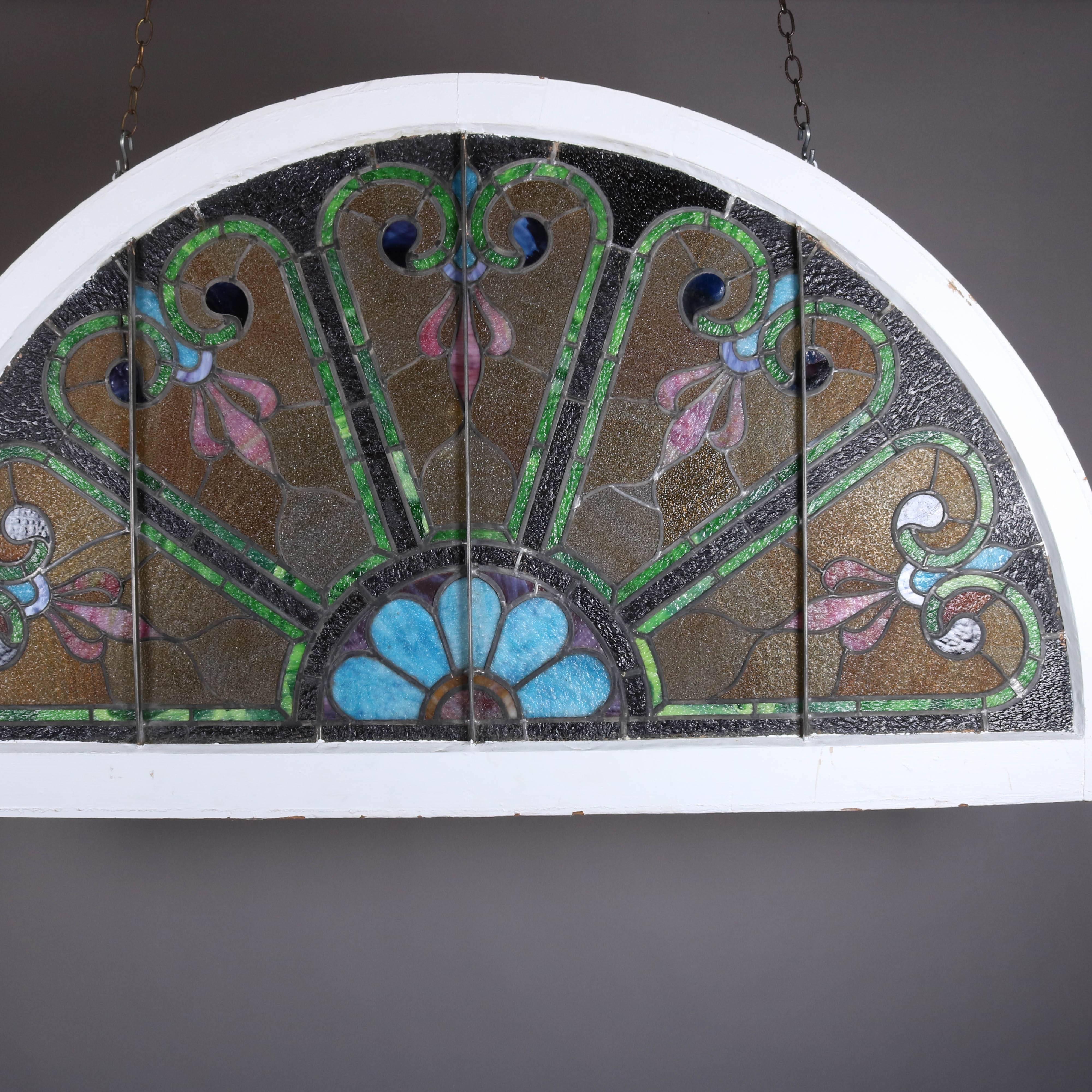 Antique stained and leaded glass arched transom window features stylized floral and scroll design panels in demilune form and seated in original wood frame, 19th century

Measures: 68