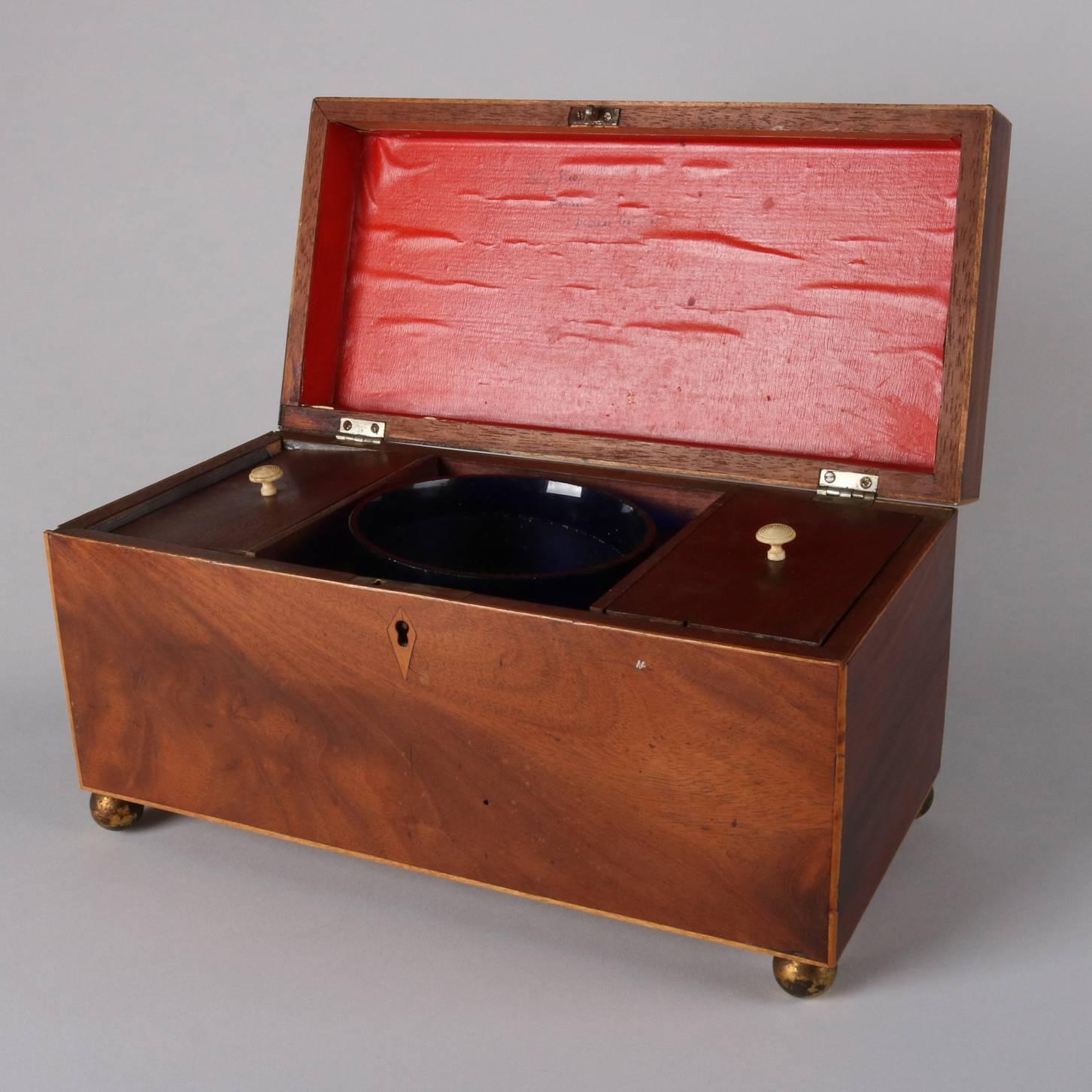Antique English Edwardian tea caddy features satinwood banded mahogany case, two lidded tea compartments with central cobalt blue glass mixing bowl, seated on gilt bronze ball feet, 19th century (inscribed 
