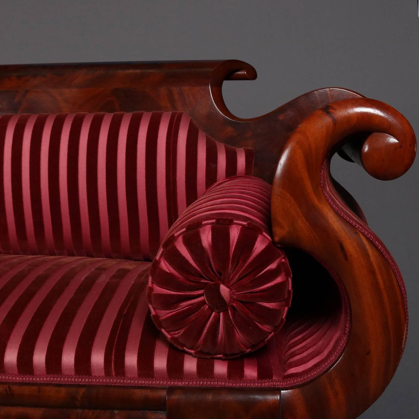 Antique Classical Empire sofa by Joseph Meeks & Co. features flame mahogany frame with scroll arms, feet and crest, covered in maroon striped upholstery, reminiscent of Quervelle, 19th century.

Measures: 33