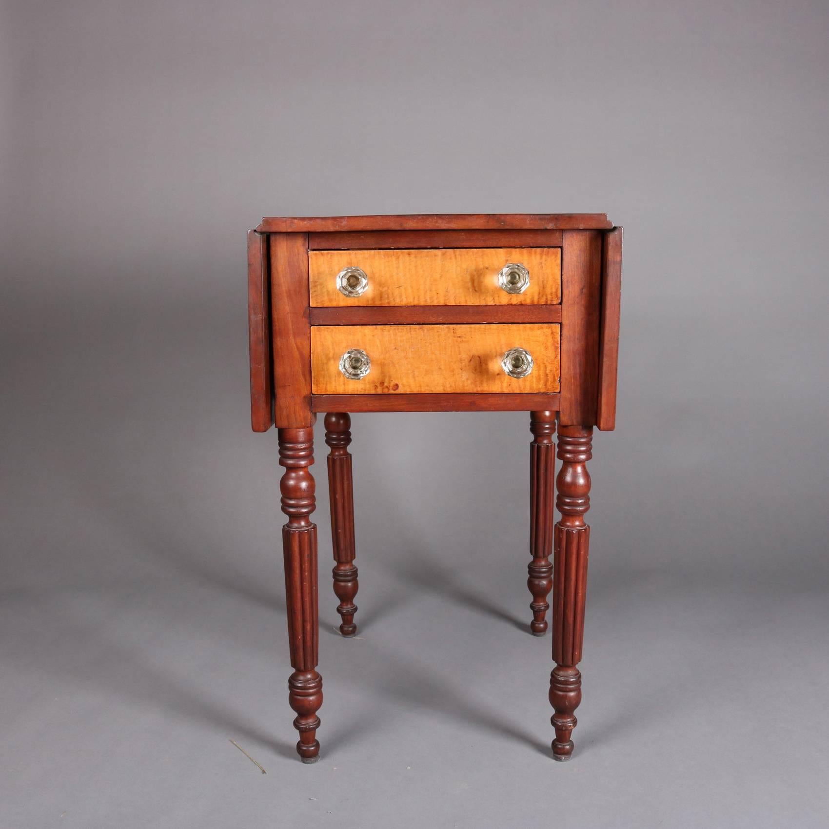 Antique Sheraton drop leaf stand features cherry construction with two tiger maple drawers with molded glass knobs and is seated on turned and reeded legs, 19th century.

Measures: 29