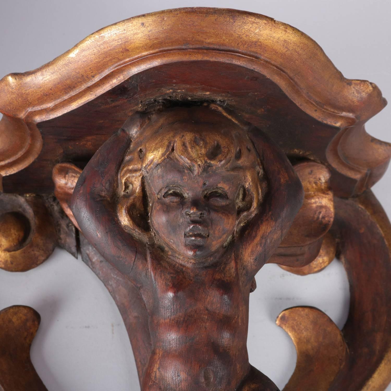 Pair of antique Italian Baroque figural gesso and carved wood candle sconces feature scroll form back with winged cherub supporting candle display platform, painted with gilt highlights, 19th century.

Measure: 13.5