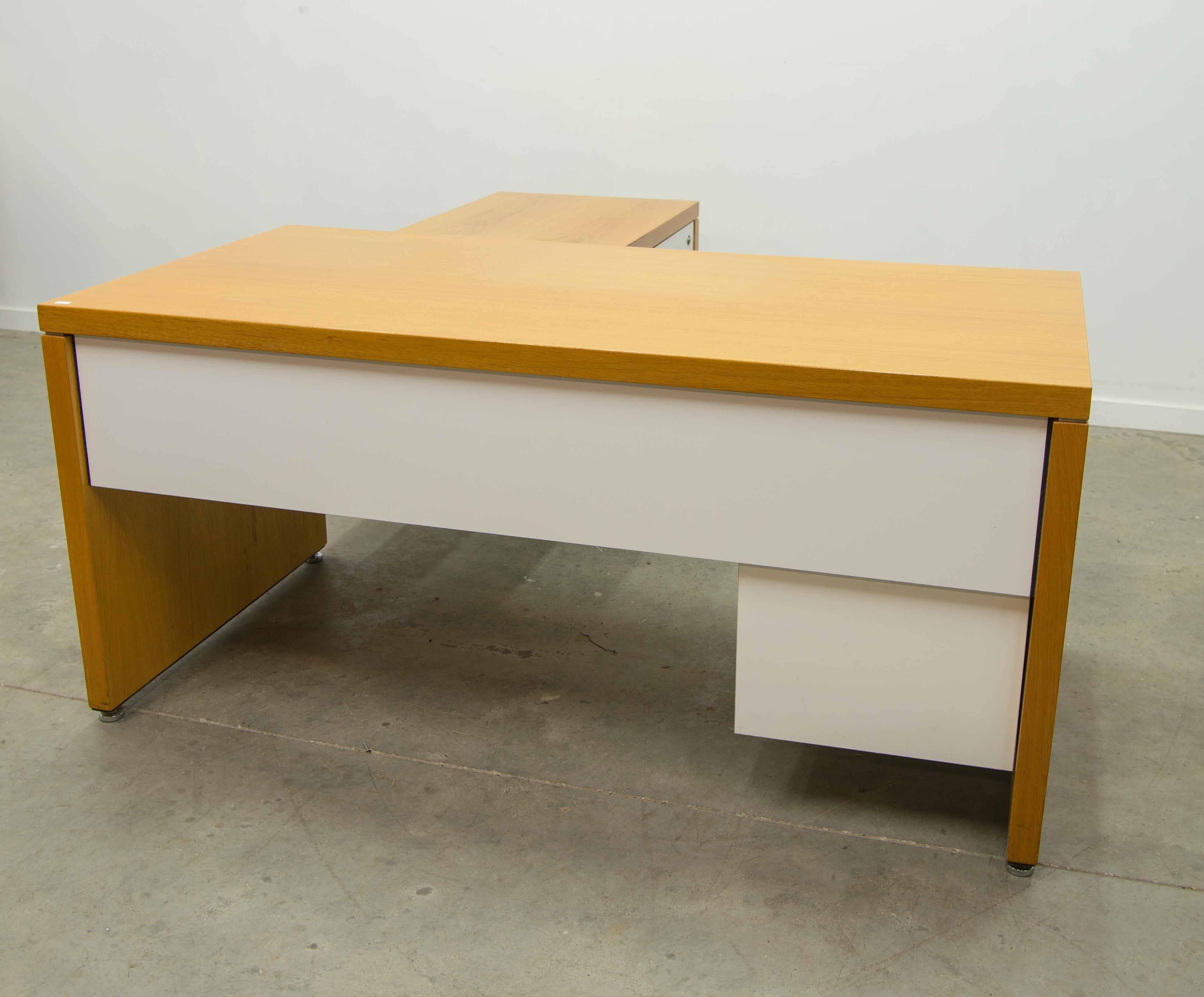 We have this desk set by William Stephens for Knoll. The set is made of two parts with different heights. There is a chrome edge separating the feet from the top. There are white room dividers on the table and a white drawers set. The drawers show