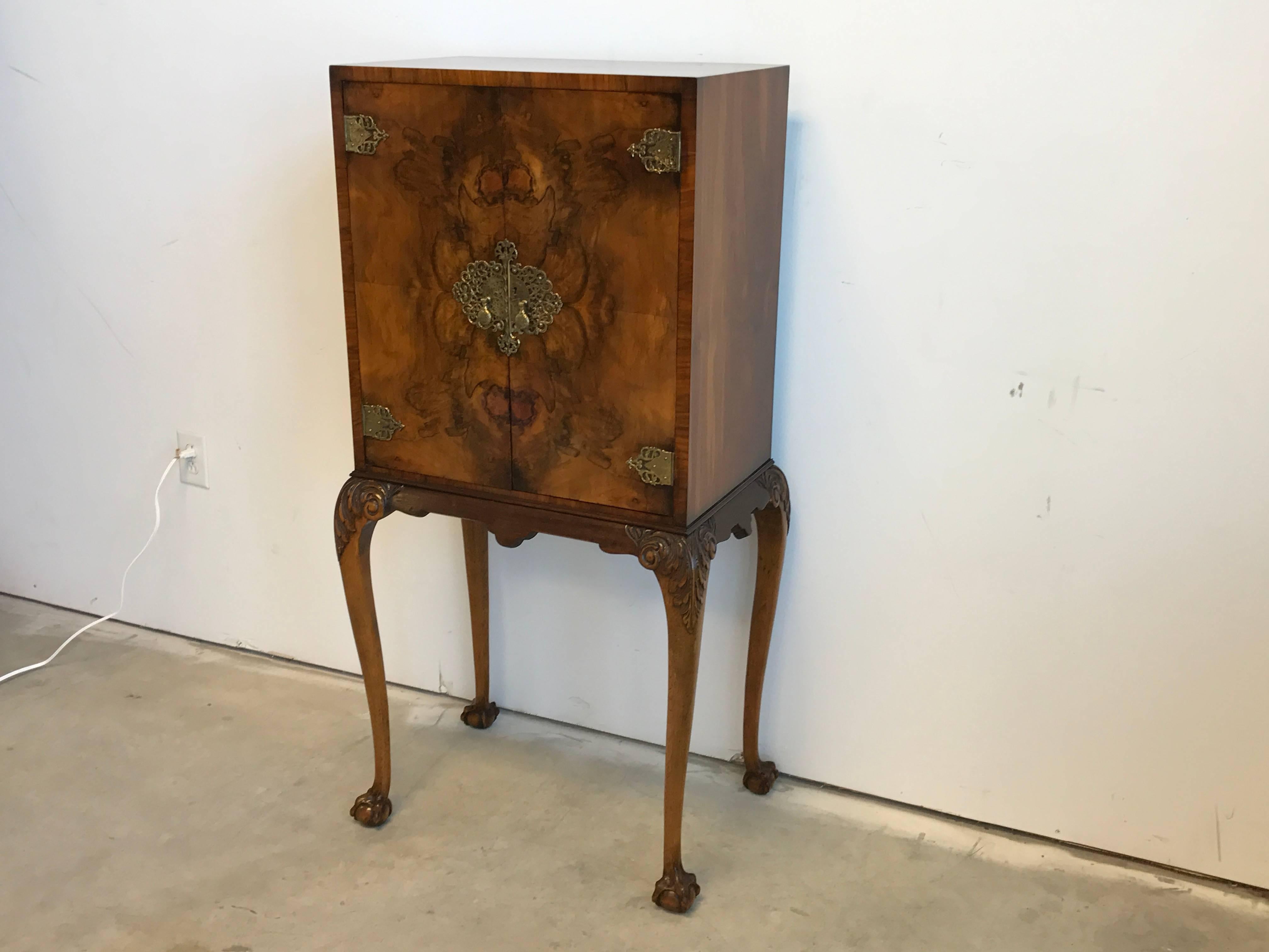 Offered is an absolutely stunning, 19th century maple-burl wood bar cabinet. This piece is a showstopper with its gorgeous and ornate brass detailing and claw feet detailing. Inside has an upper rack for glasses, beneath is a glass and wood serving